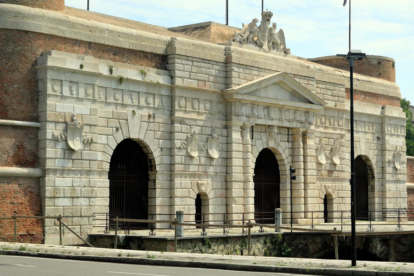 The outer front of Porta Nuova, the 16th-century city gate of Verona, in pale stone with arched openings and a sculpted crest on top.