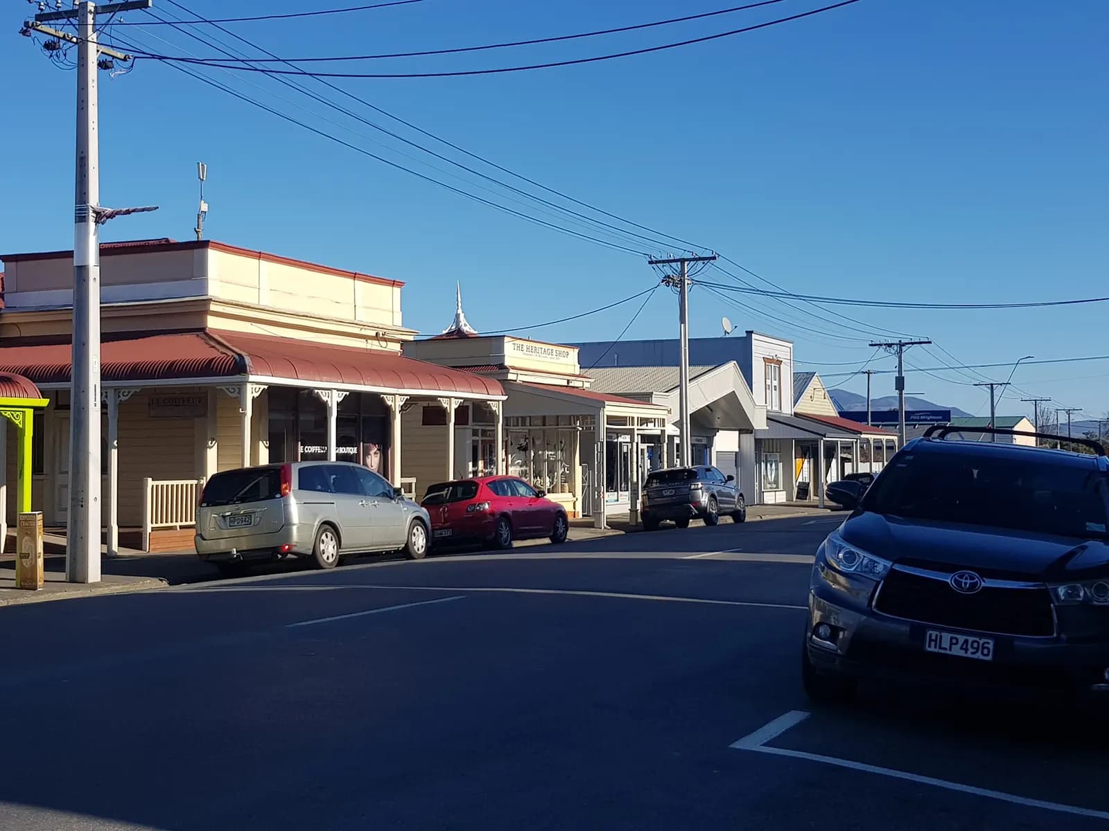 Single-storey shops with verandas on Jellicoe Street in Martinborough, with cars parked along the street under a clear sky