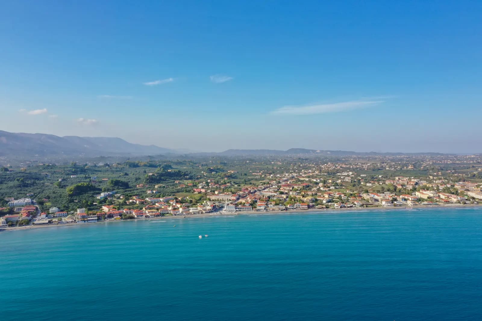 Aerial view of Laganas on Zakynthos, with hotels and houses behind the long sandy beach of Laganas bay and green hills beyond