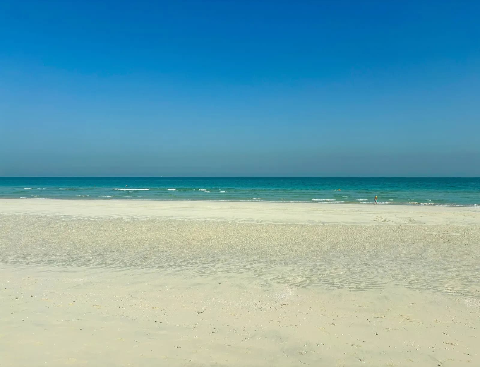 A wide, almost empty white sand beach on Saadiyat Island in the morning, with small waves on turquoise water