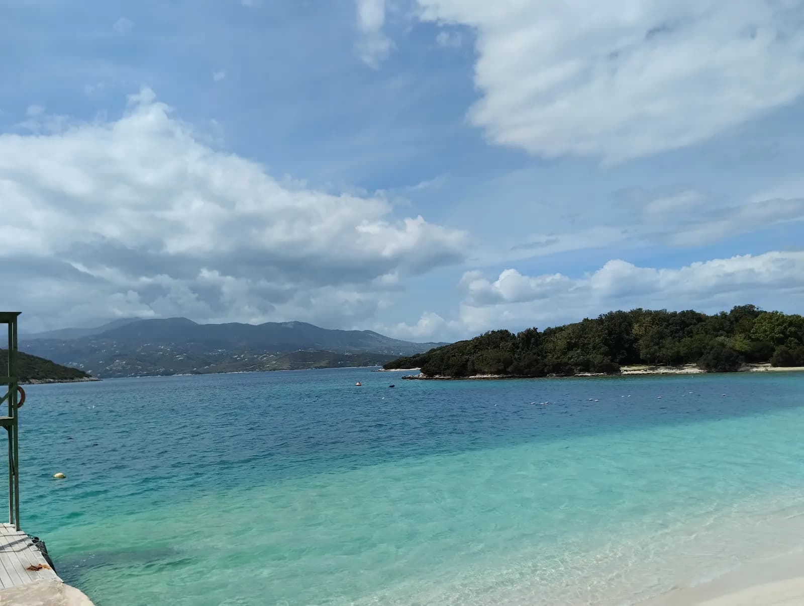 Clear turquoise water off a beach at Ksamil, with one of the wooded Ksamil islets and the hills of Corfu across the strait