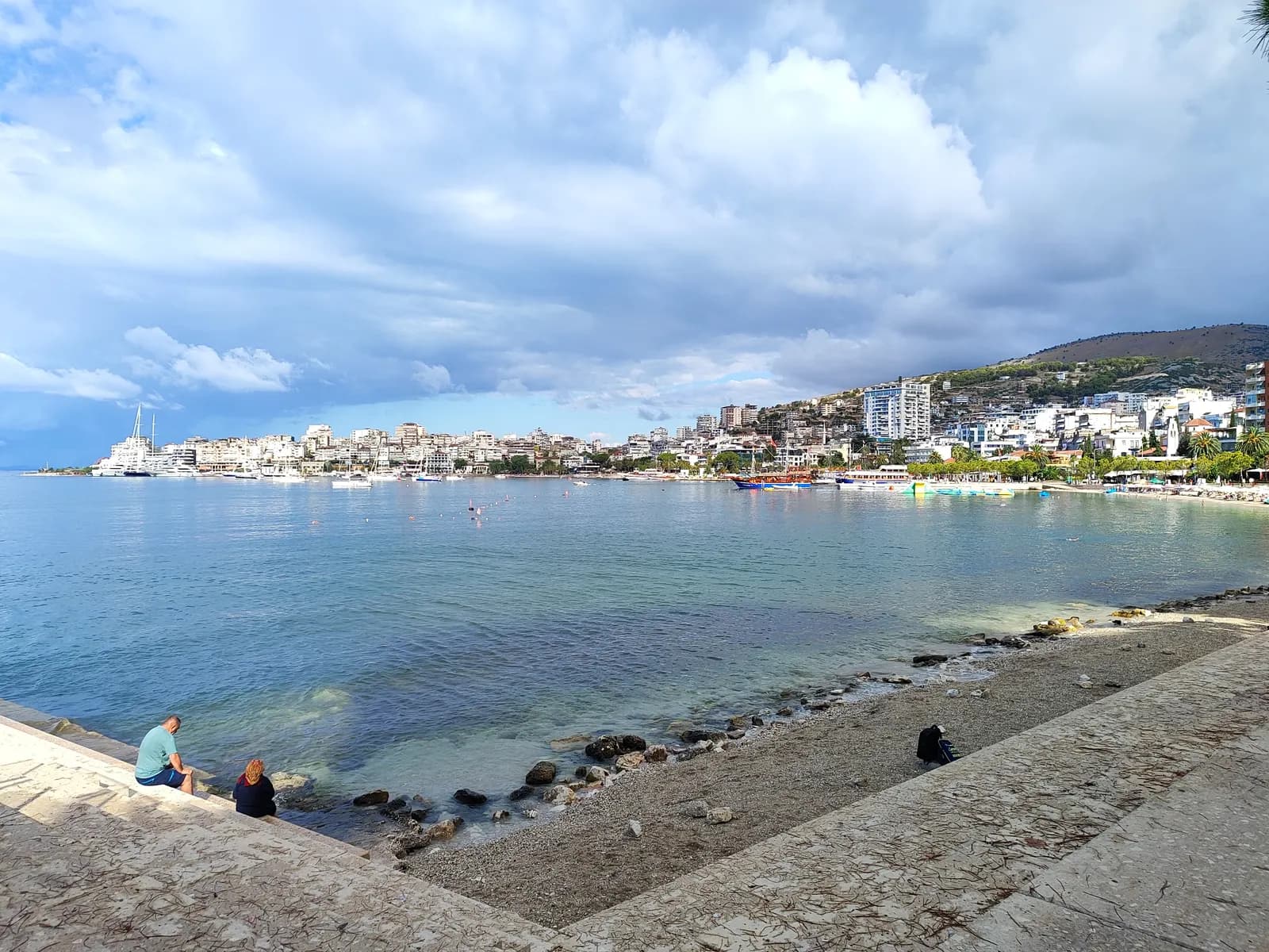 The public beach below the seafront promenade in Sarandë, with the town and its apartment blocks around the bay
