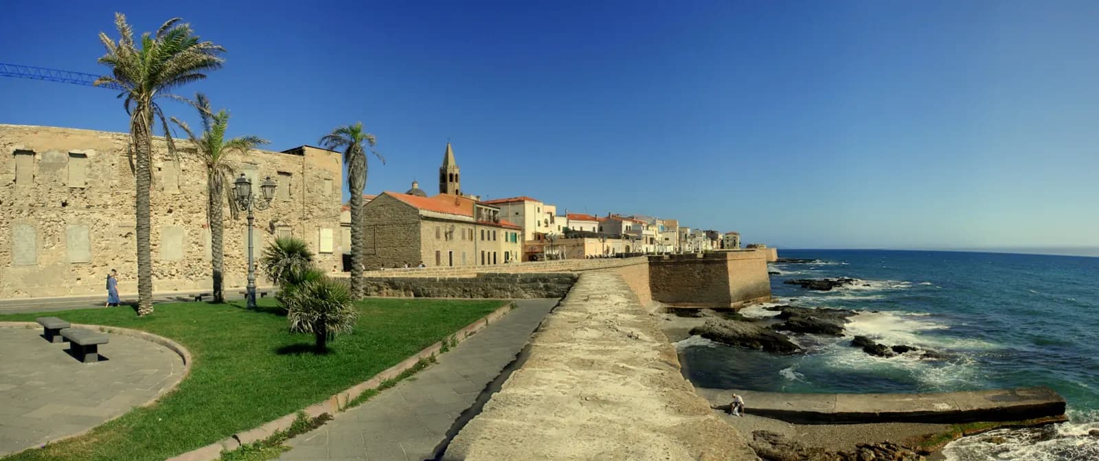 The walled front of Alghero from the bastions, with palms, the cathedral bell tower above the roofs and the sea on the right