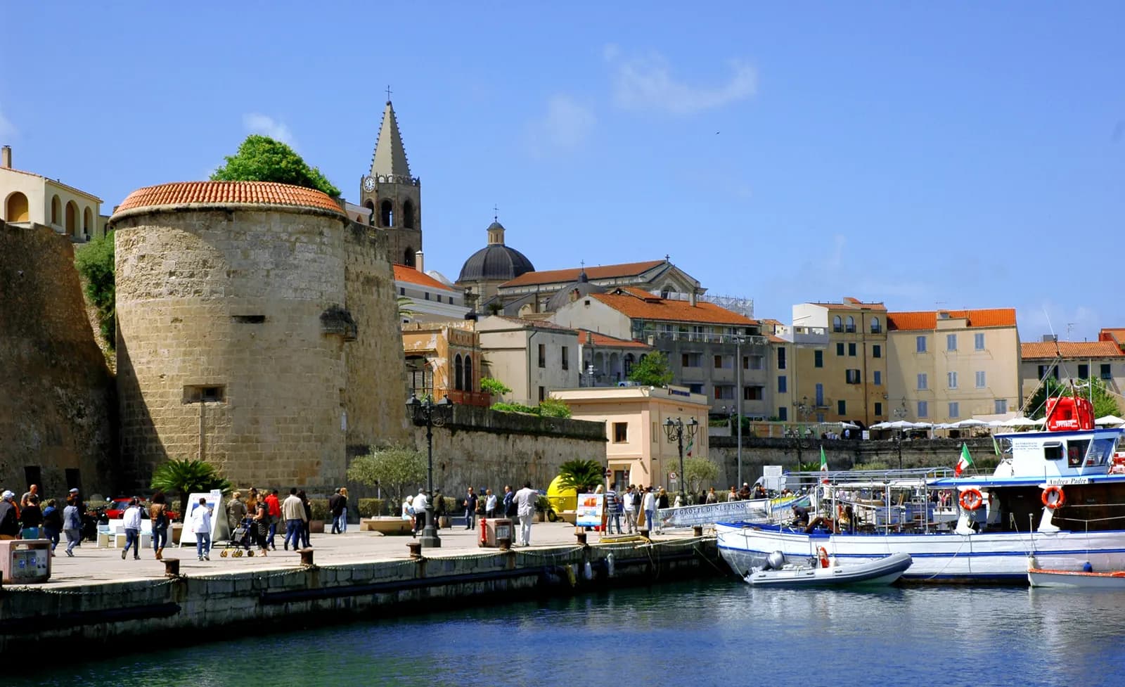 The quay at Alghero with fishing boats, the round Torre Sulis and the bell tower and dome of the old town behind