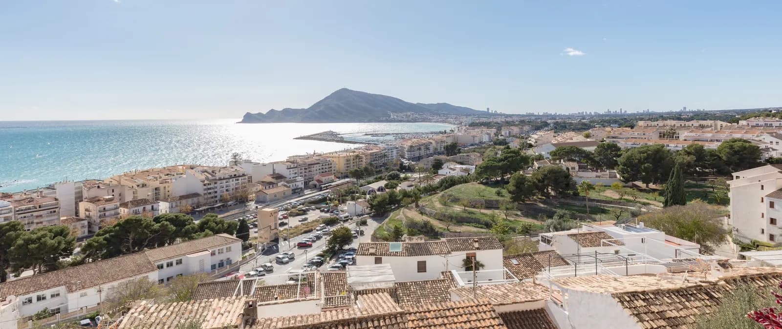 Altea seen from the old town, with tiled roofs in the foreground, the seafront, the marina and the Serra Gelada headland across the bay.