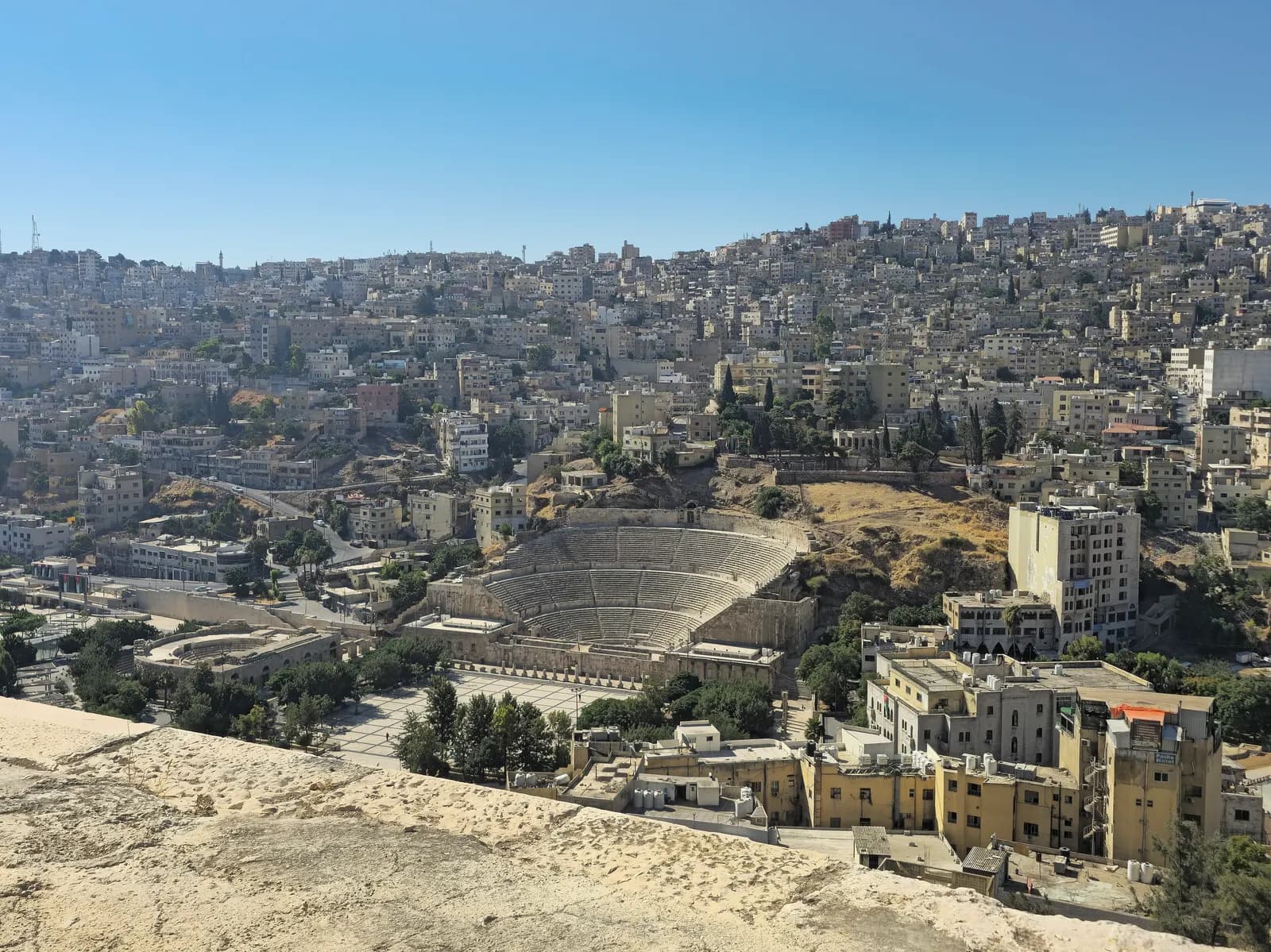 Downtown Amman seen from the Citadel hill: the Roman theatre and its paved plaza in the valley, with pale stone houses covering the hillside behind