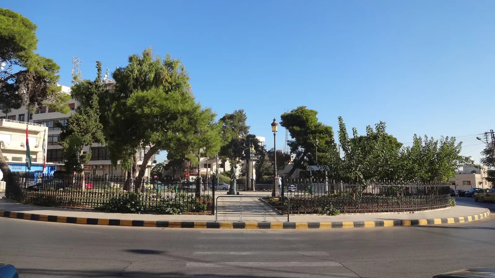 Paris Circle in Jabal al-Weibdeh, a fenced garden roundabout with pine trees, street lamps and a green fountain in the middle