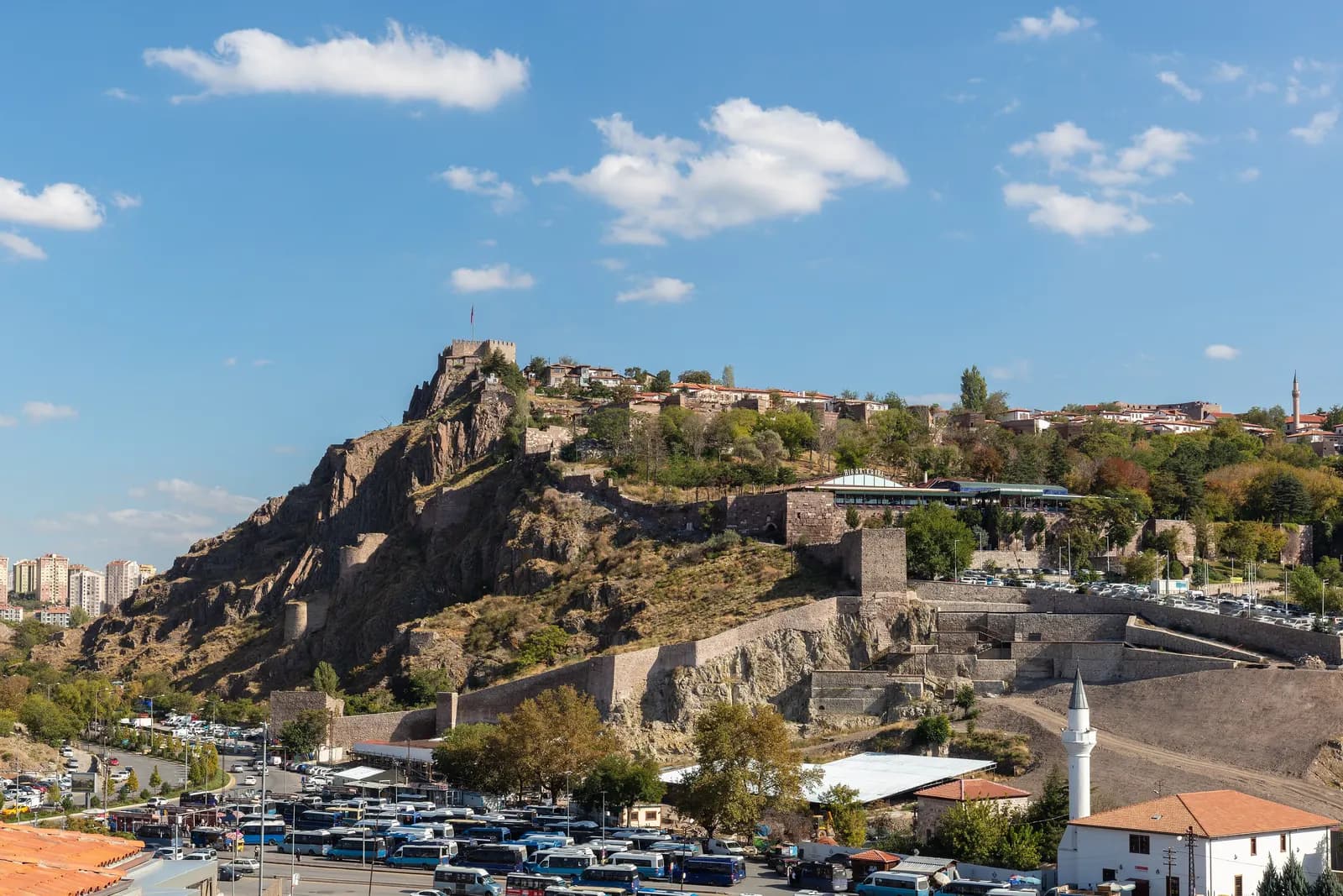 Ankara Castle on its rock above the old city walls, with houses along the ridge and rows of parked buses and cars below