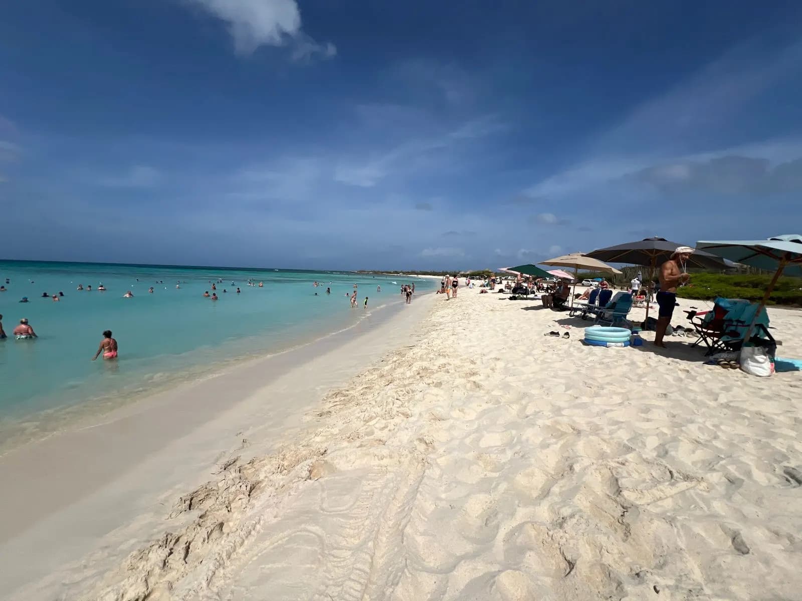Arashi Beach at the north end of Aruba's west coast, with shallow turquoise water, swimmers and beach umbrellas on the sand