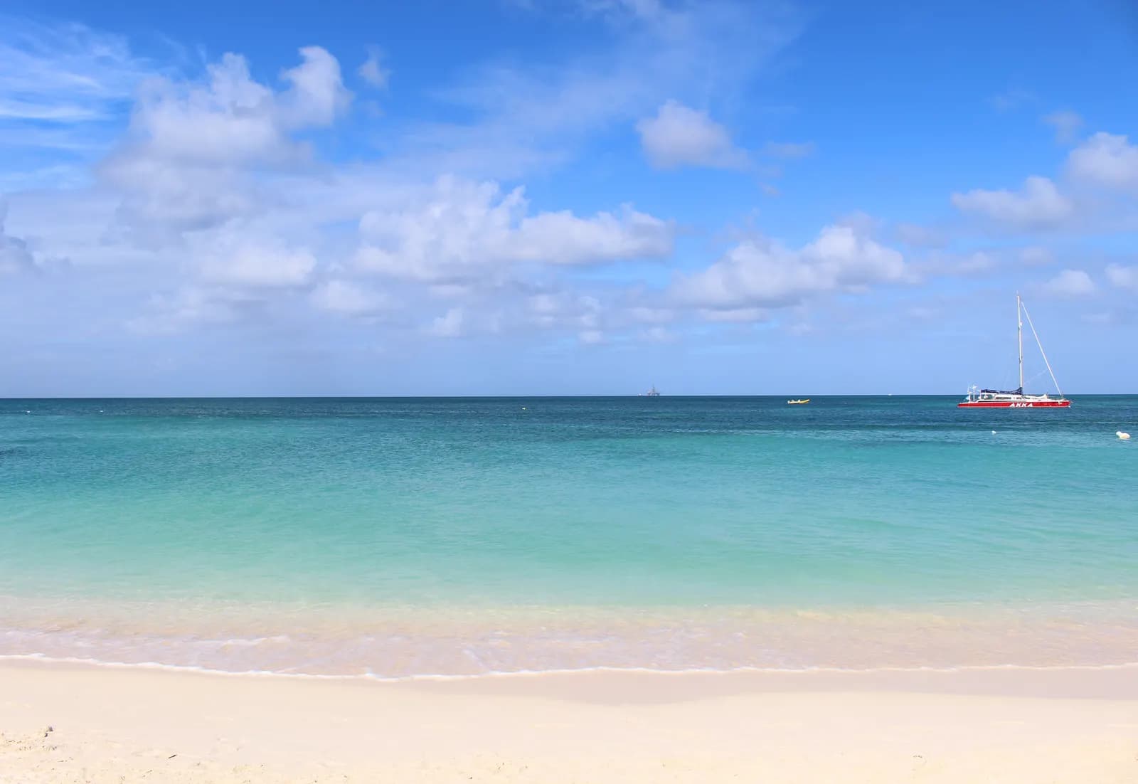 Turquoise water and white sand at Palm Beach, Aruba, with a catamaran on the sea under a blue sky with clouds