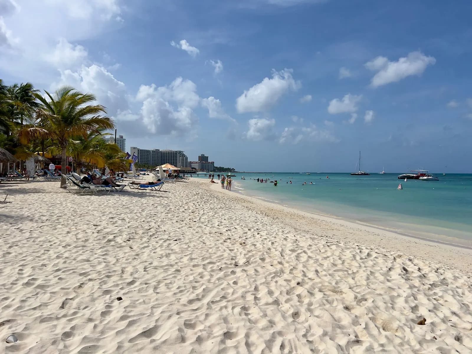 Palm Beach in Aruba with rippled white sand, palm trees and sun loungers, and hotel towers along the shore in the distance