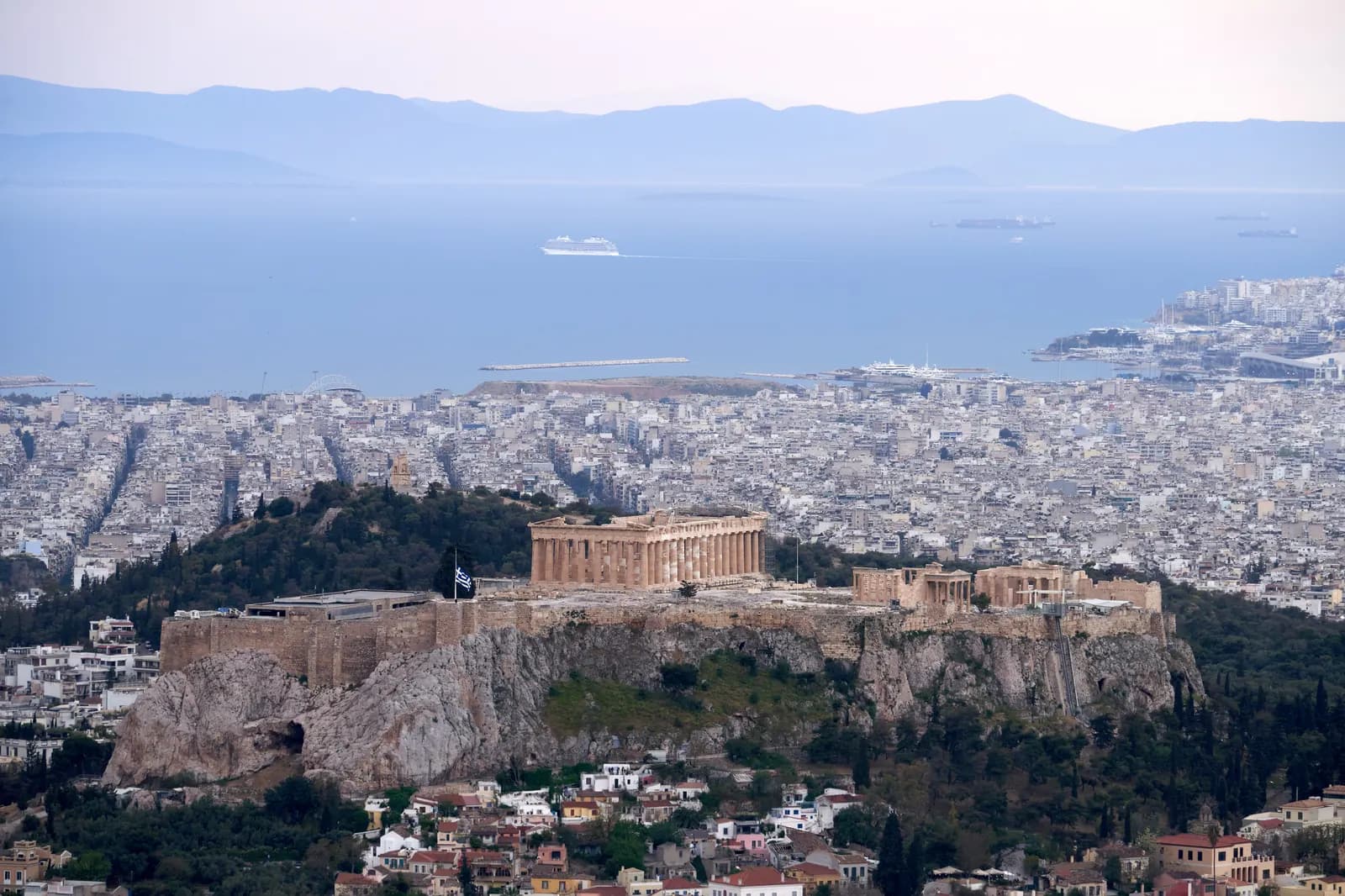 The Acropolis and the Parthenon on their rock above the white apartment blocks of Athens, with the Saronic Gulf and the Peloponnese mountains beyond