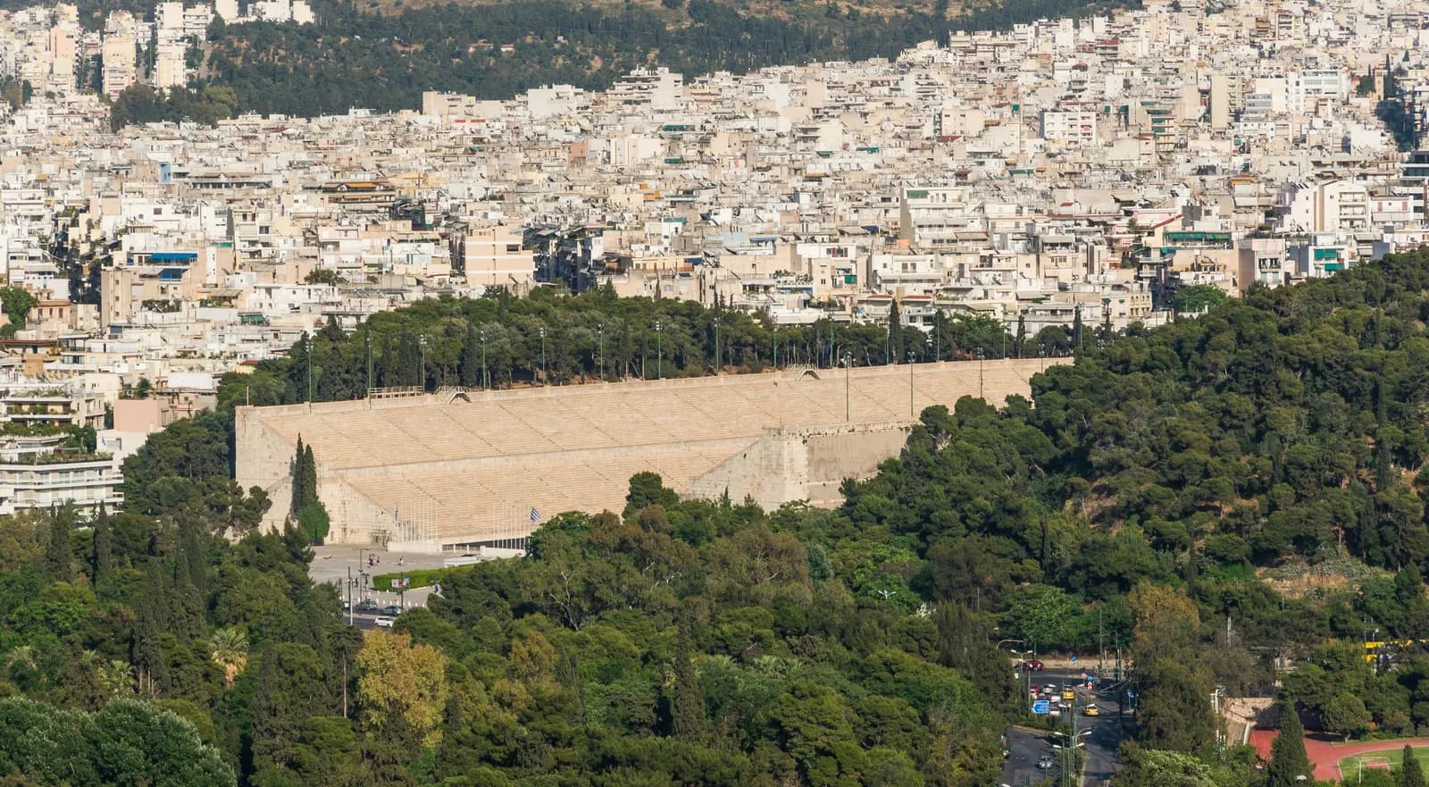 The marble Panathenaic Stadium among pine trees, with the dense apartment blocks of Pangrati rising on the hill behind it