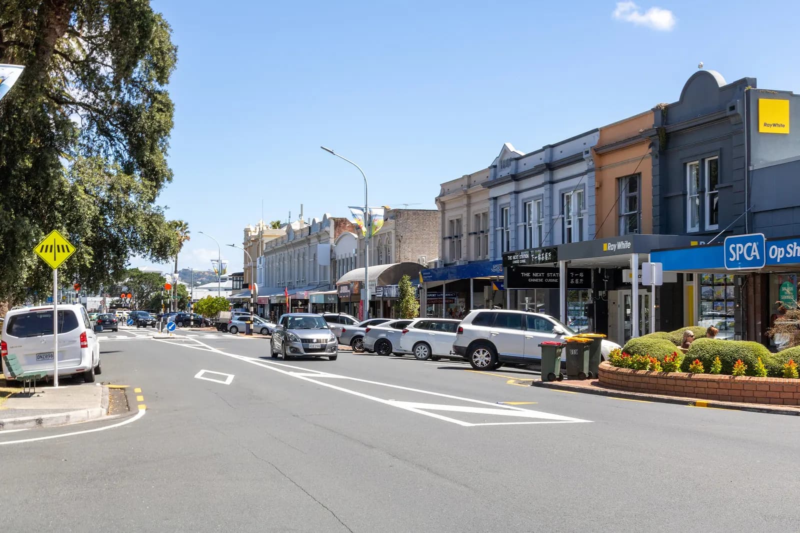 Victoria Road in Devonport with cars parked along a row of two-storey shopfronts, looking towards the ferry terminal