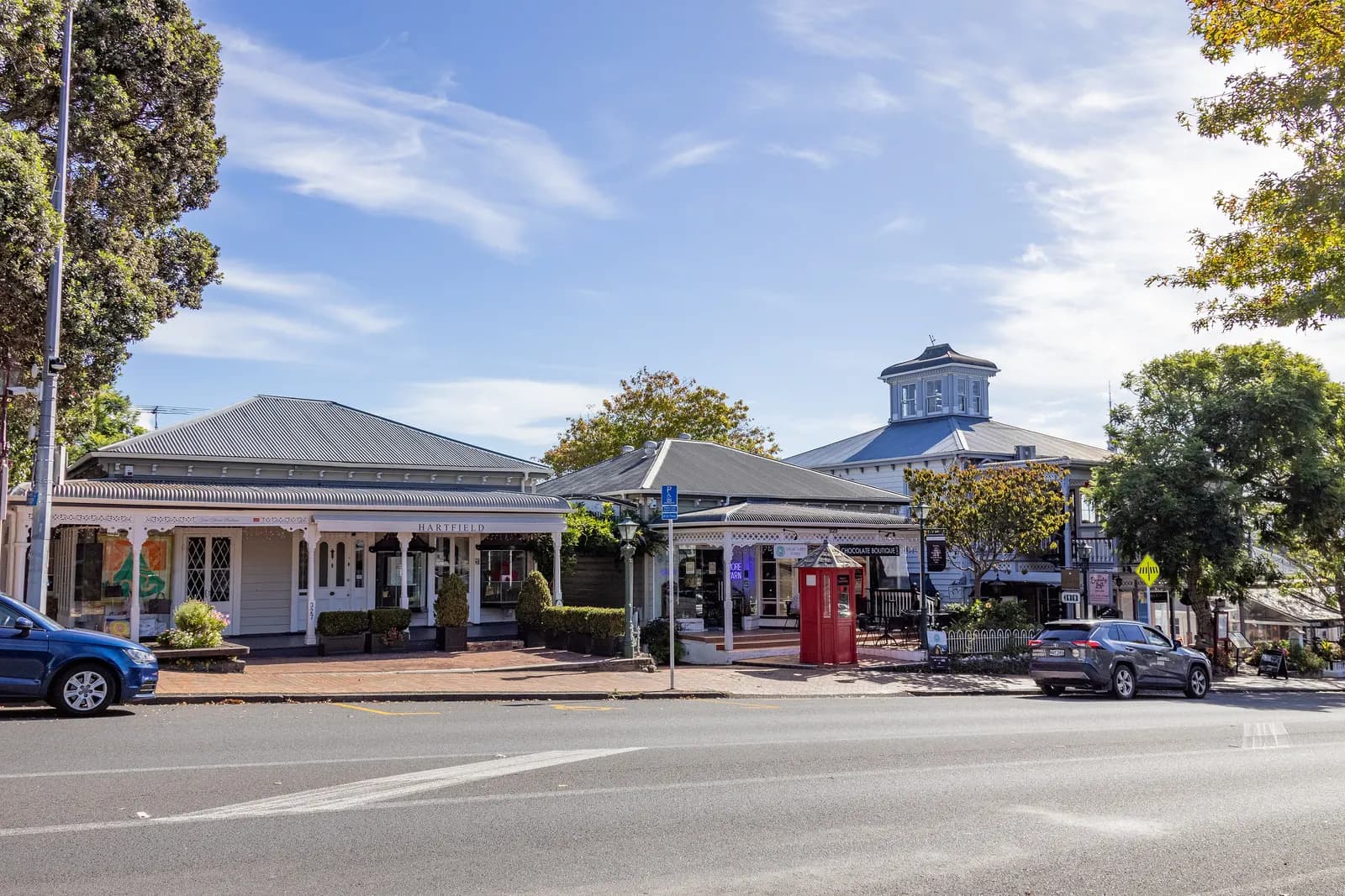 Low white wooden shopfronts with verandas at Parnell Village, seen from across Parnell Road, with a red telephone box and parked cars