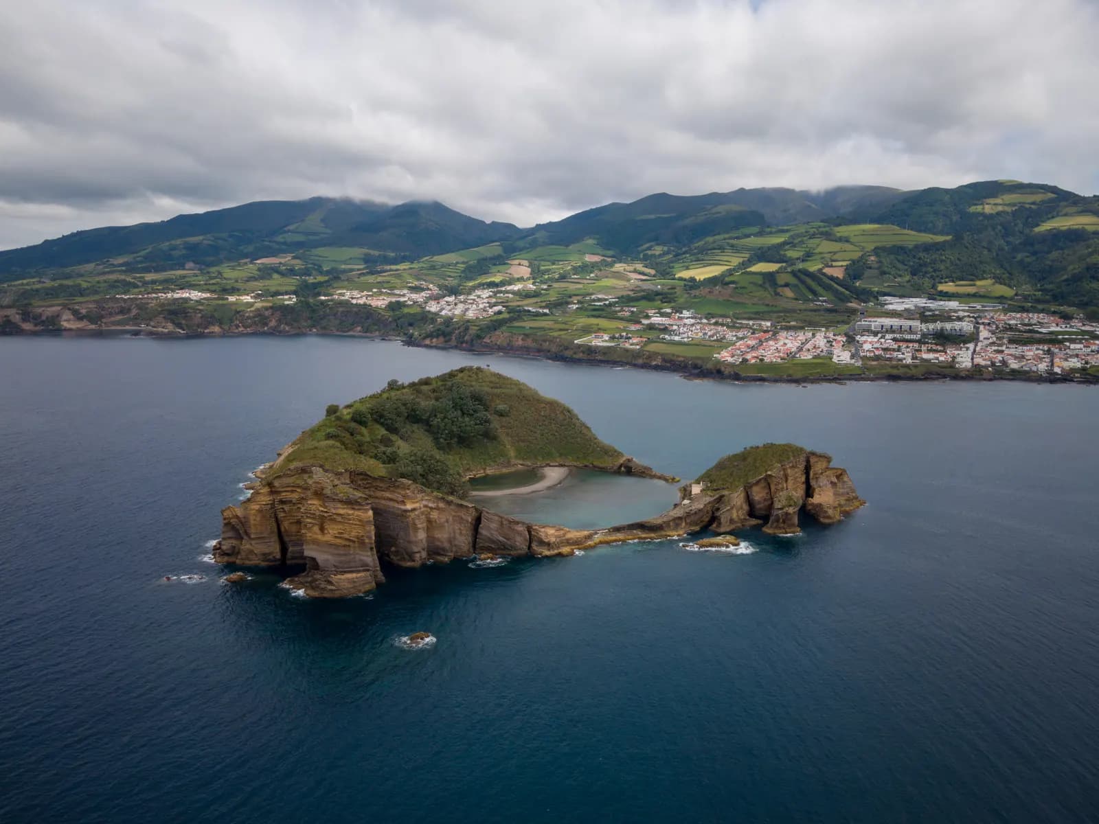 Aerial view of the Vila Franca islet, a small crater with a round pool inside, and the town of Vila Franca do Campo on the coast behind