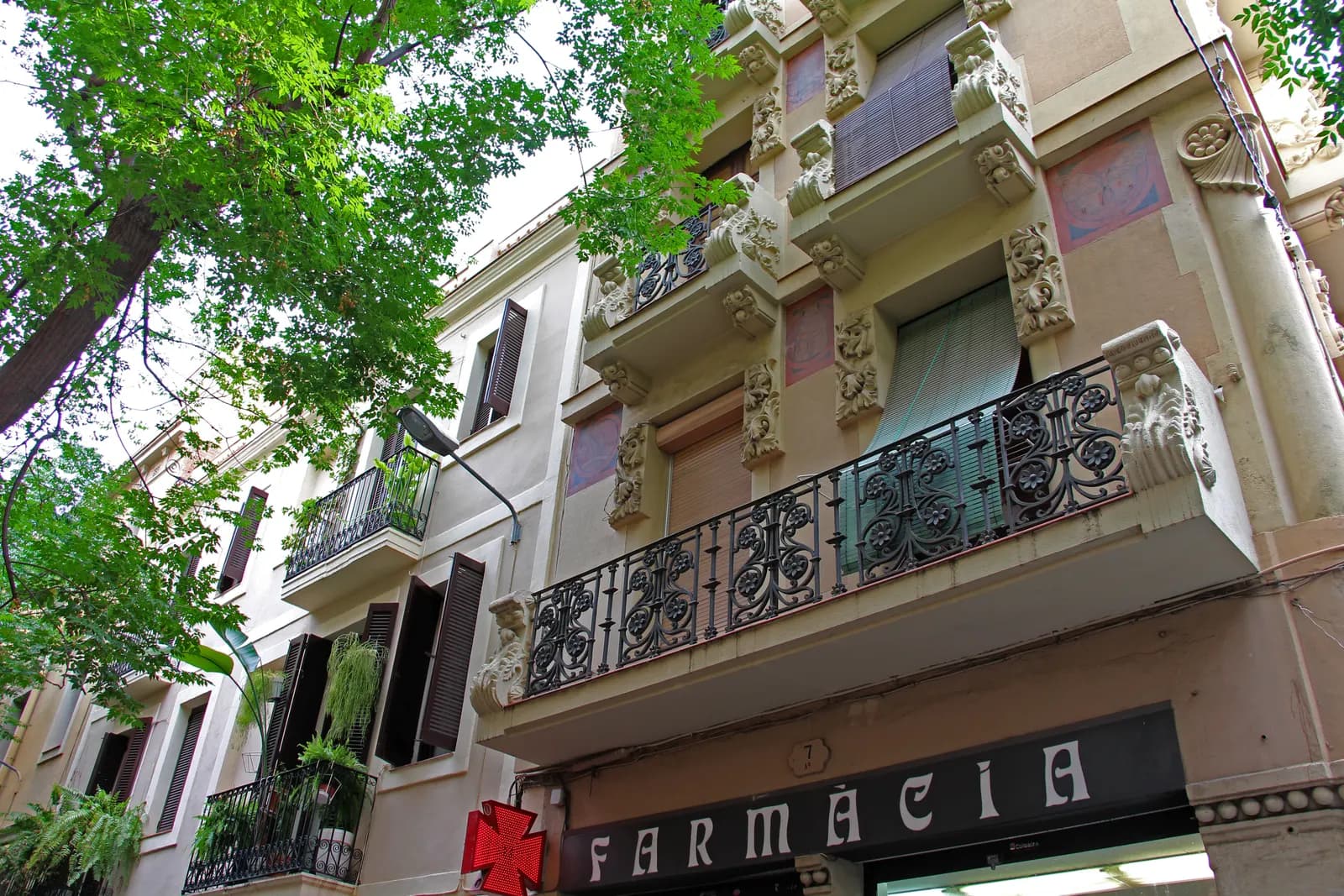 Modernista balconies and a corner pharmacy on Carrer de Verdi in Gràcia, framed by street trees.