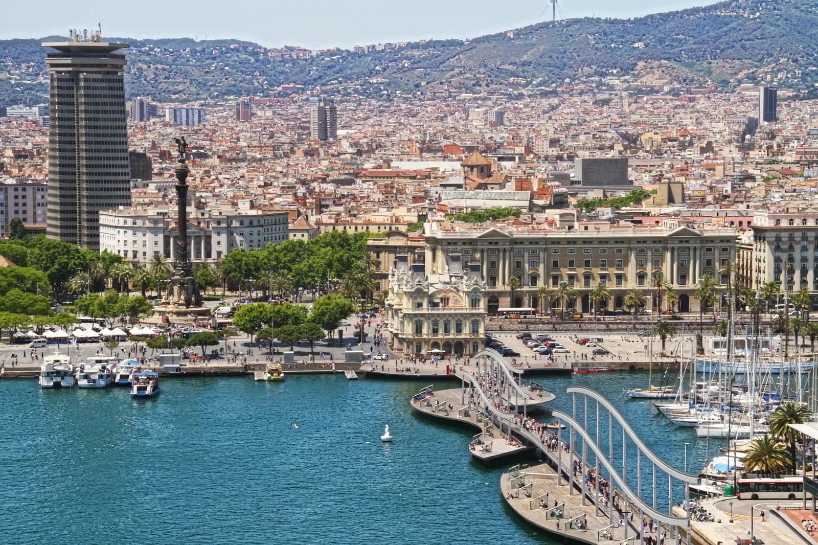 Barcelona seen from the port cable car: Port Vell, the Columbus monument and the Rambla de Mar footbridge, with the city spreading to the Collserola hills.