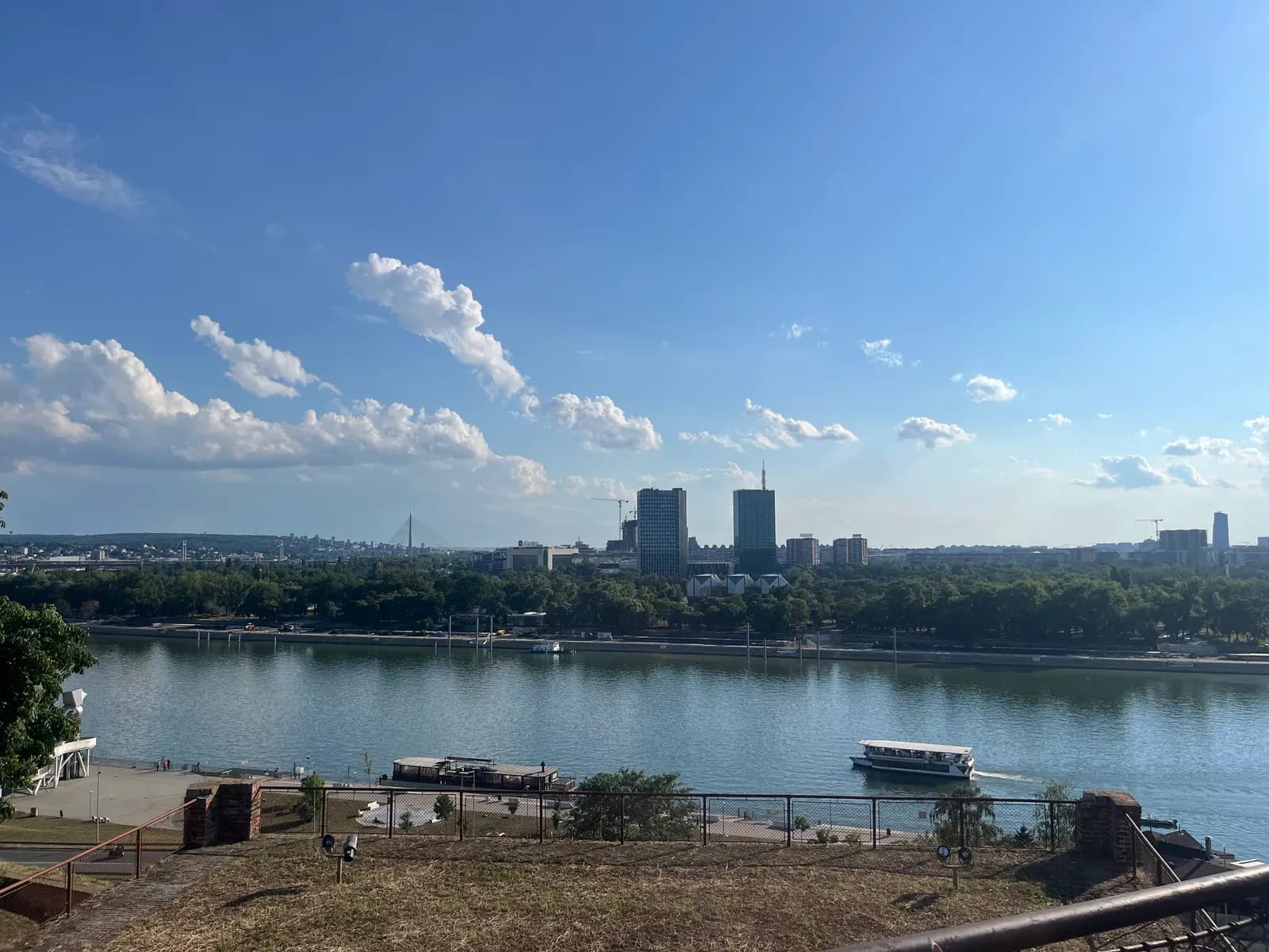 The Sava river seen from Kalemegdan in Belgrade, with a tourist boat on the water and the towers of New Belgrade behind the trees on the far bank
