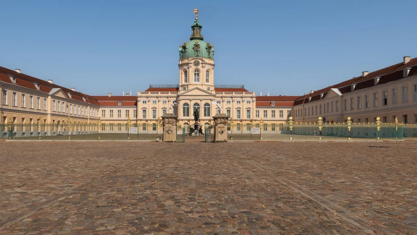 Charlottenburg Palace with its green dome and gilded railings, seen across the cobbled forecourt under a clear sky
