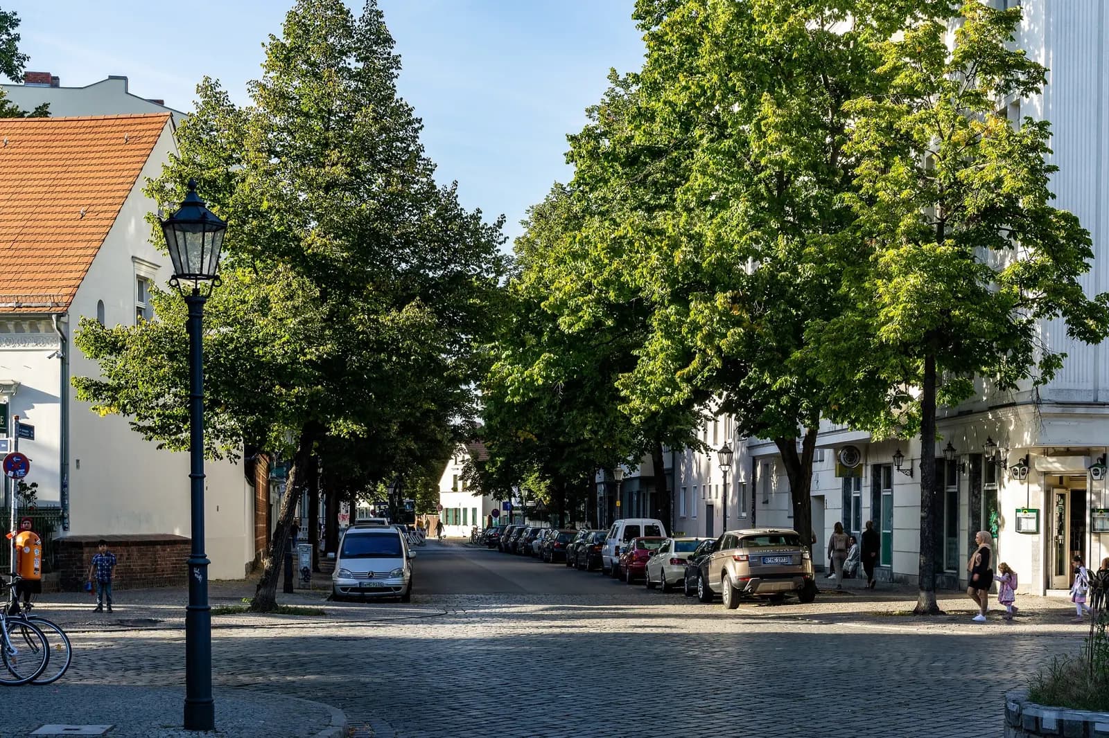 A tree-lined cobbled street in Böhmisch-Rixdorf by Richardplatz in Neukölln, with cars parked along it and low houses under lime trees