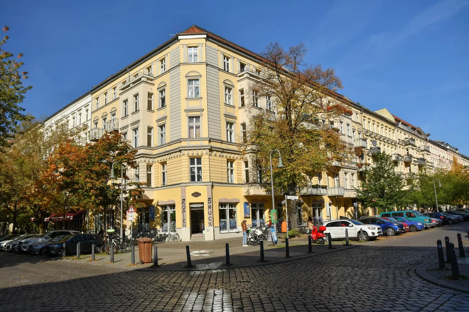 Cobbled crossing of Wörther Straße and Rykestraße in Prenzlauer Berg, with tenement blocks, autumn trees and cars parked along the kerb