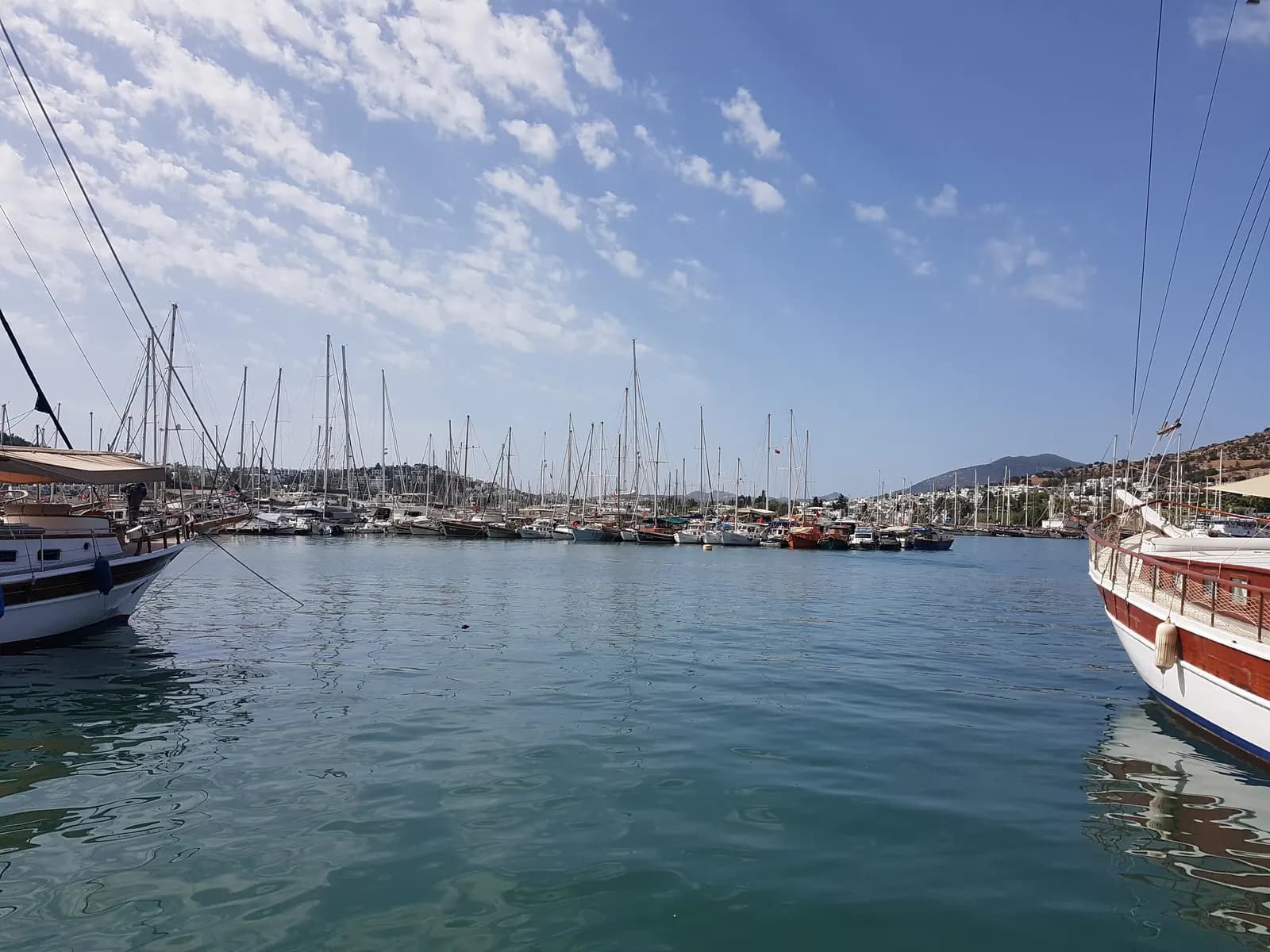 Rows of yachts and wooden gulets in Bodrum marina, with white houses on the hills around the bay