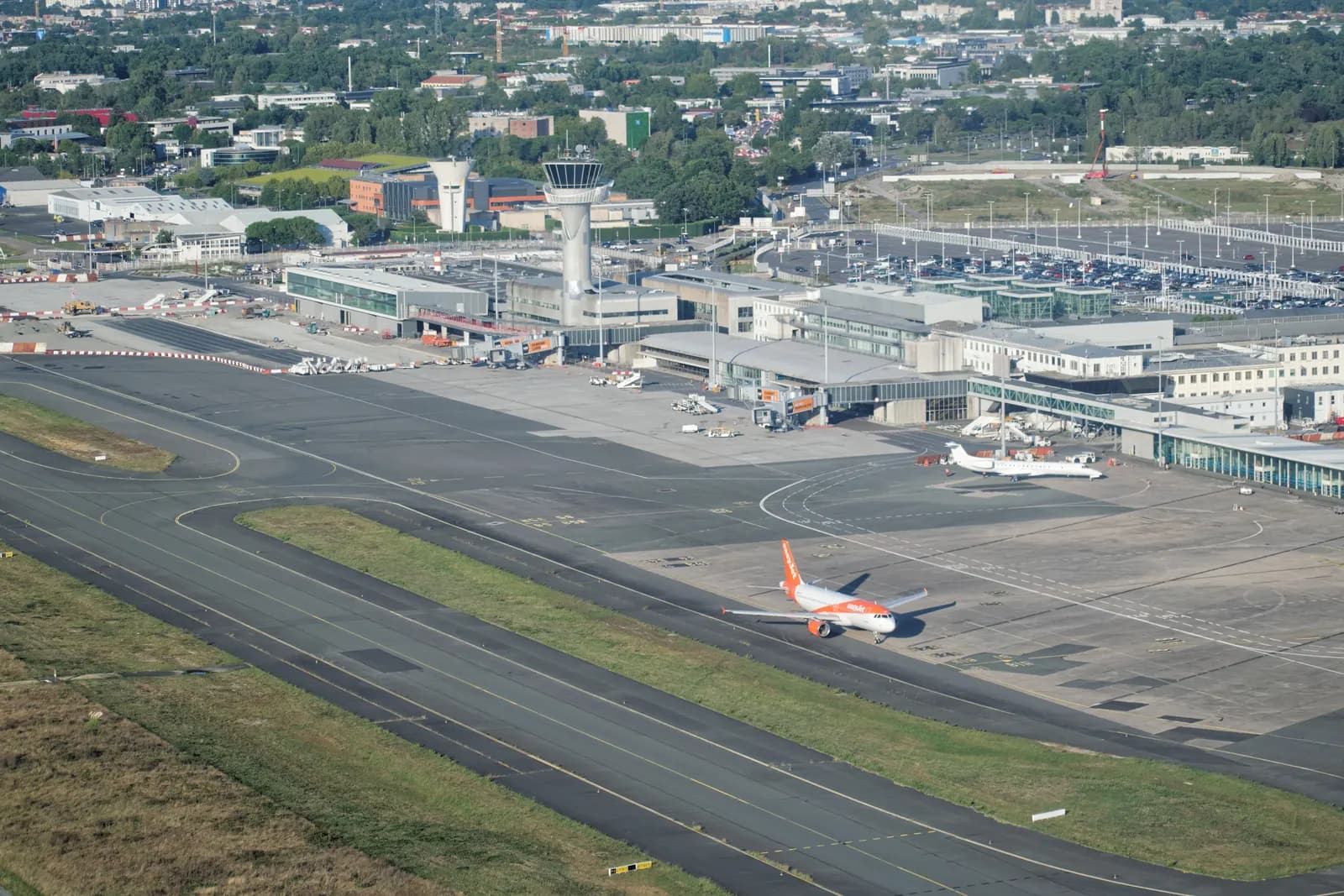 Bordeaux Mérignac airport from the air, with the control tower, the terminals, the car parks behind them and an airliner on the taxiway