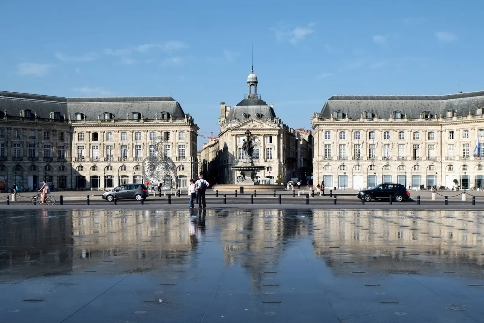 The Place de la Bourse in Bordeaux reflected in the miroir d'eau water mirror, with traffic passing on the quay between them