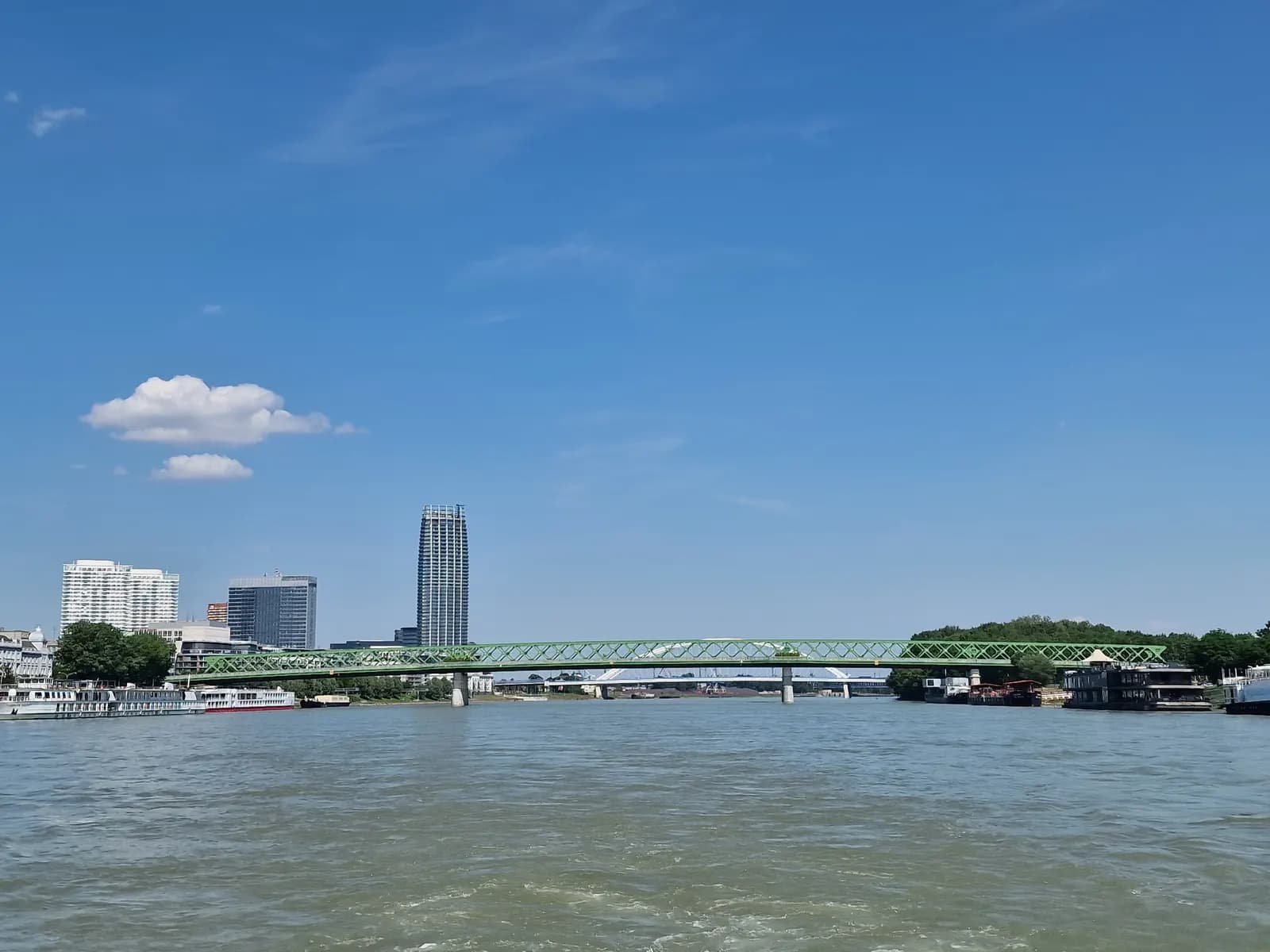 The Danube in Bratislava seen from the water, with the green truss of the Old Bridge and high-rise towers on the left bank