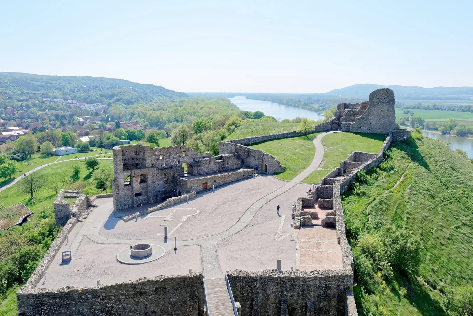 The ruins of Devín Castle seen from above, with stone walls, a paved courtyard, the village of Devín on the left and the river behind