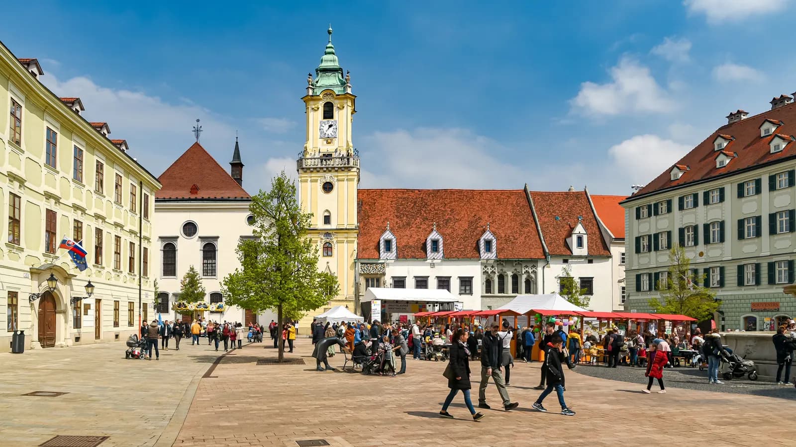 Hlavné námestie, the main square of Bratislava old town, with the yellow tower of the Old Town Hall, market stalls and people walking on the paving