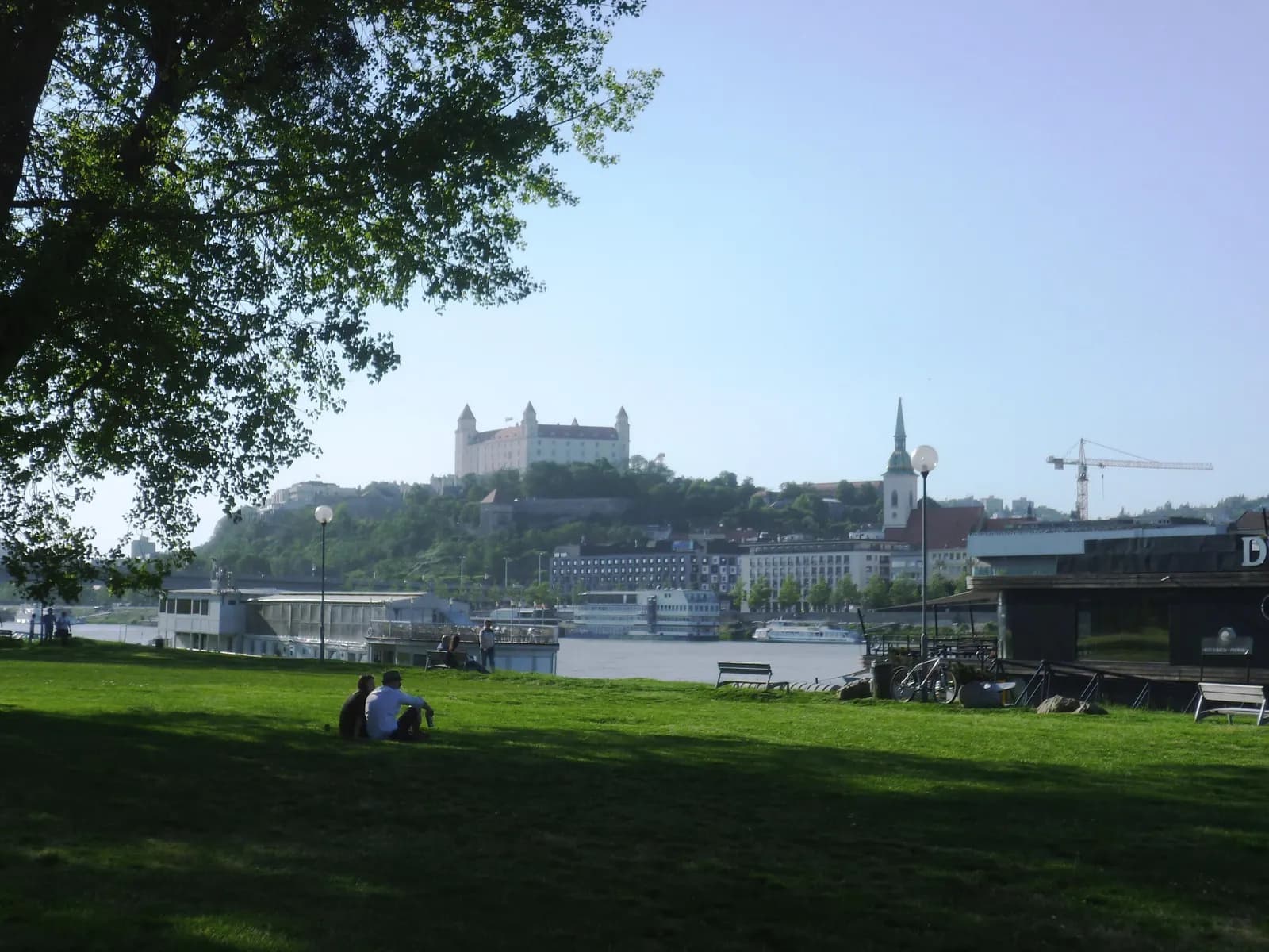 A lawn by the Danube in Sad Janka Kráľa park, Petržalka, with Bratislava Castle and the spire of St Martin's Cathedral across the river