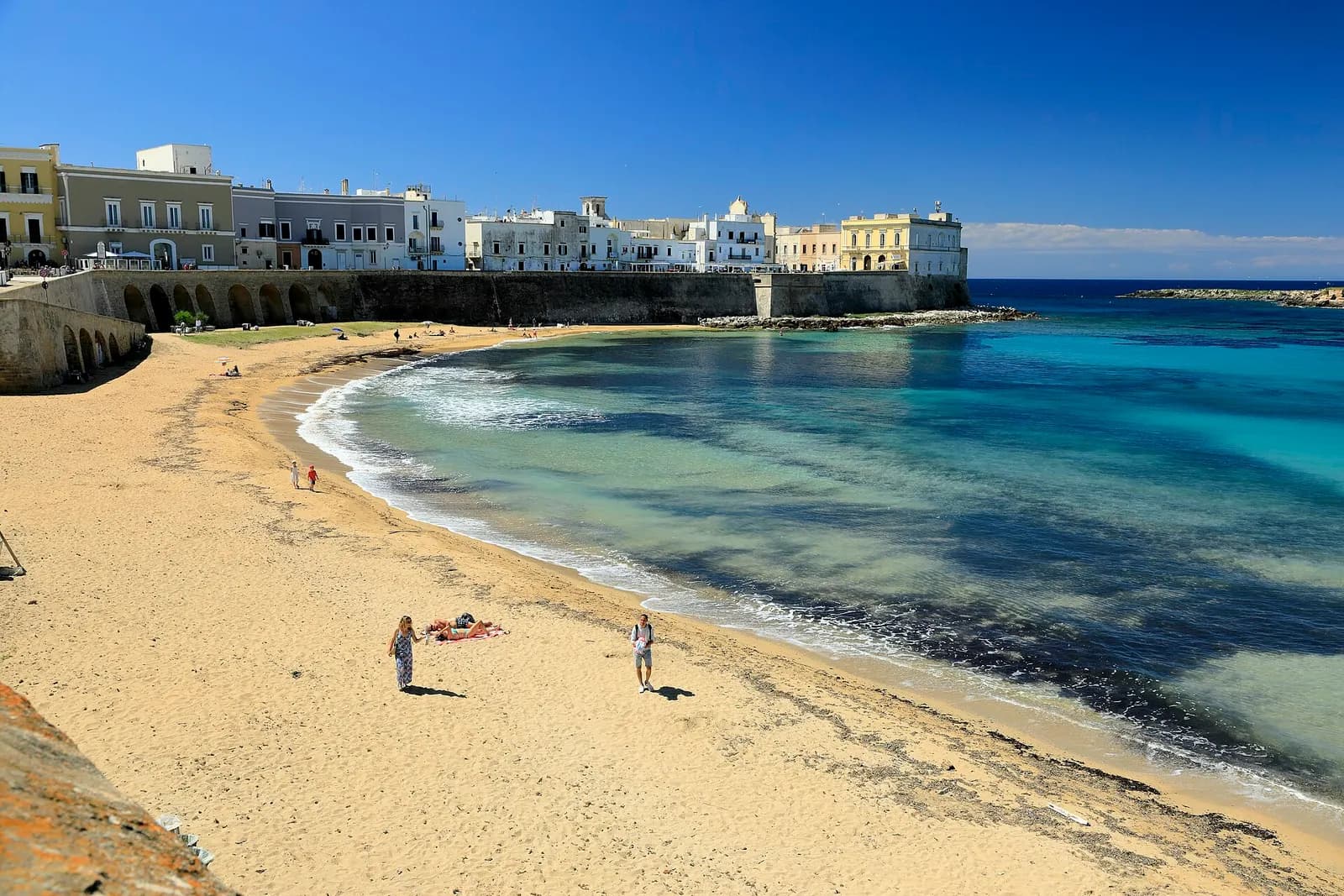 The Purità beach below the sea walls of Gallipoli's old town, with a curve of pale sand and clear water