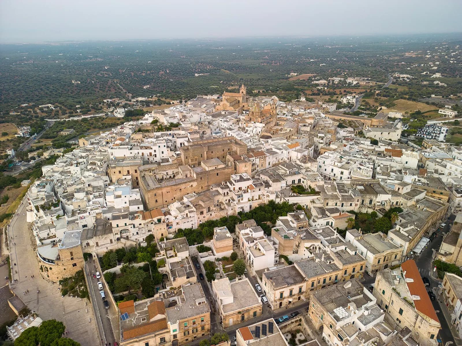 The white historic centre of Ostuni seen from the air, with the cathedral at the top of the hill and olive groves beyond