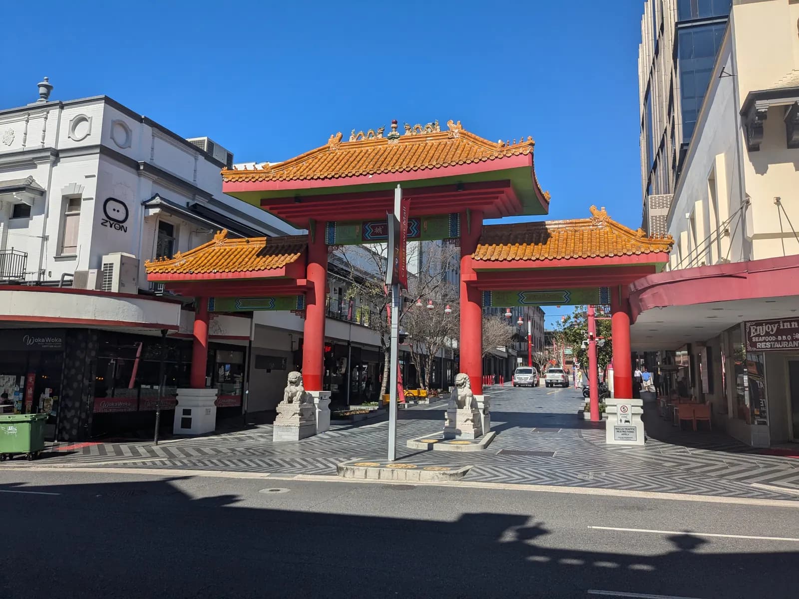 The Chinatown gate in Fortitude Valley, with red columns, orange tiled roofs and two stone lions, opening onto the Chinatown Mall between shops and restaurants