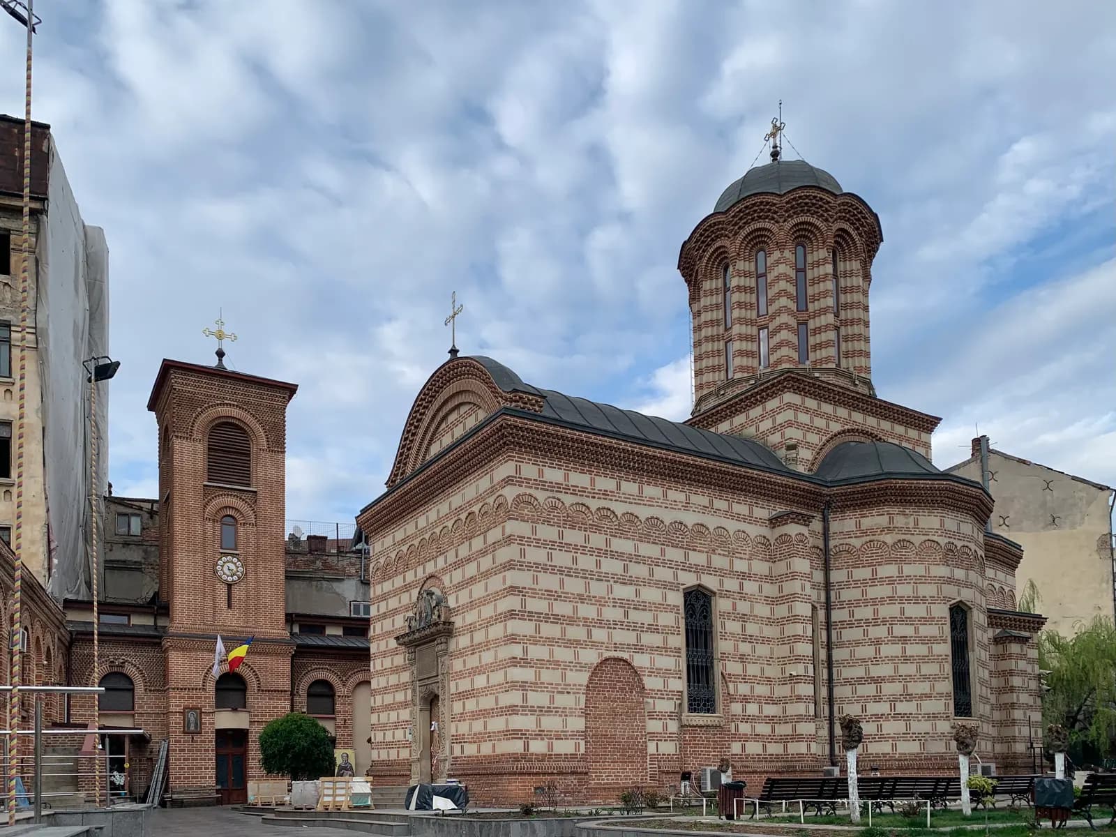 The Princely Church at Curtea Veche in Bucharest's Old Town, a striped brick and stone church with a round tower, with a brick bell tower beside it under a cloudy sky
