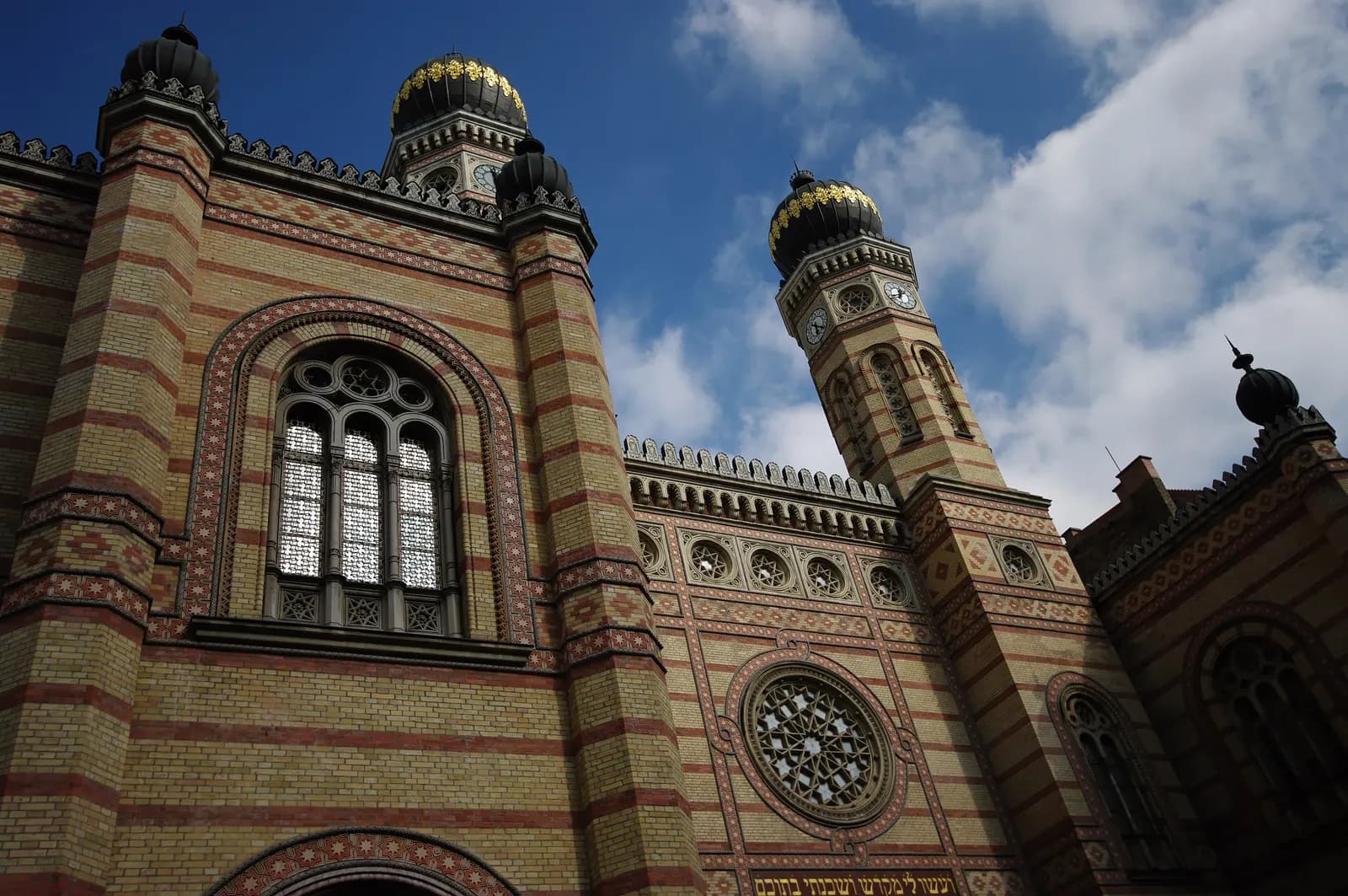 The striped brick facade of the Dohány Street Synagogue with its rose window and two onion-domed towers against a blue sky