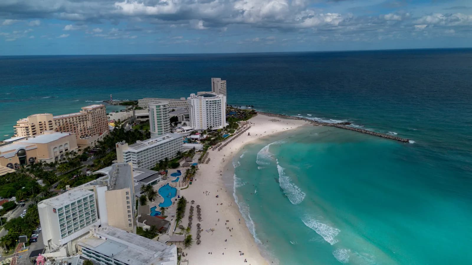Aerial view of Punta Cancún in the Hotel Zone, with hotel towers, a curved white beach and a stone jetty reaching into turquoise Caribbean water