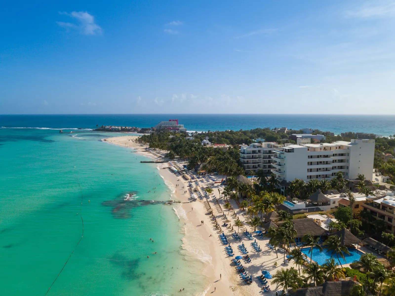 Aerial view of Playa Norte on Isla Mujeres, with shallow turquoise water, a white beach lined with sun loungers and palms, and hotels behind