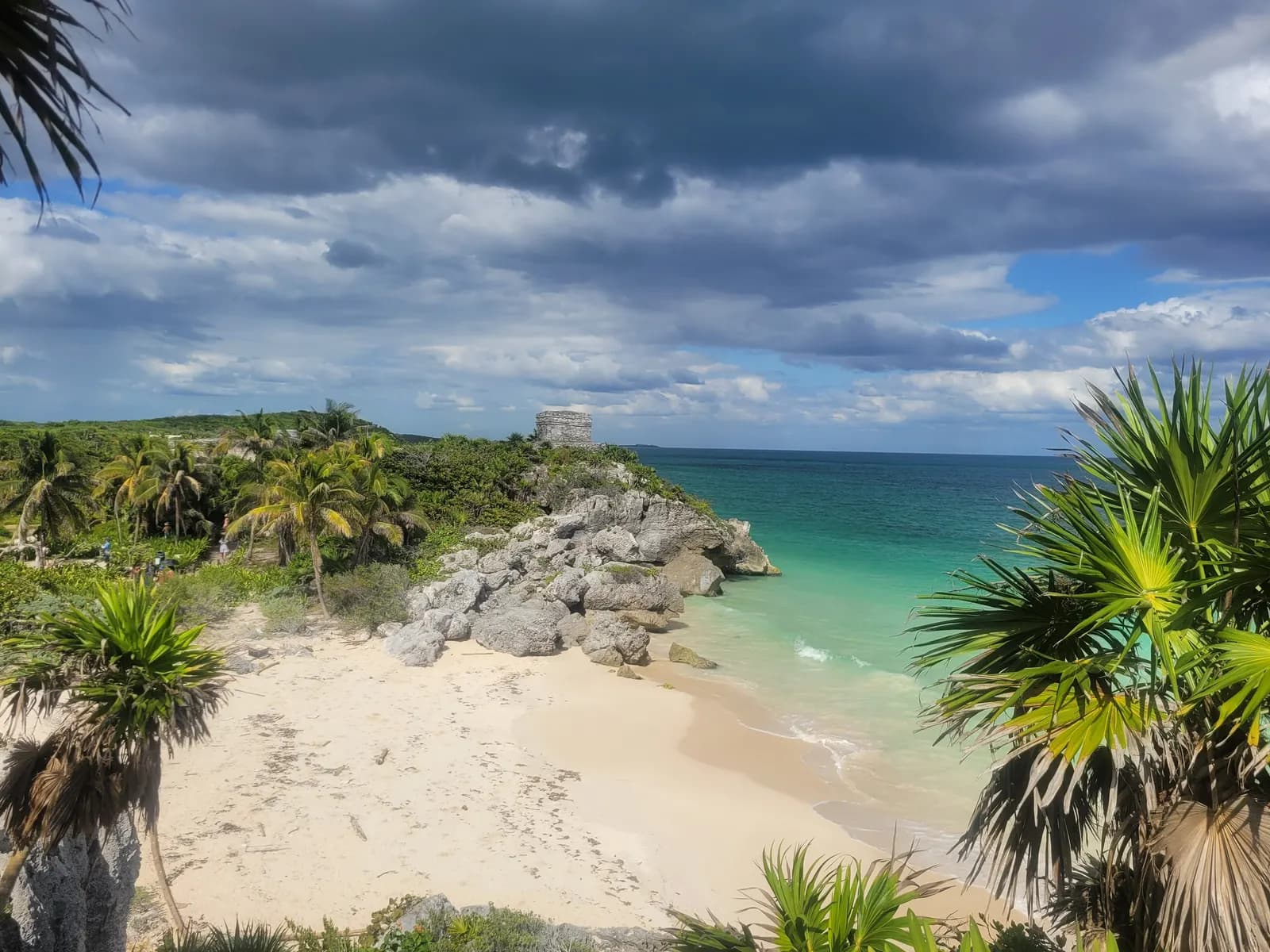 A small beach below the Tulum ruins, with a stone temple on a rocky headland, palms and turquoise sea