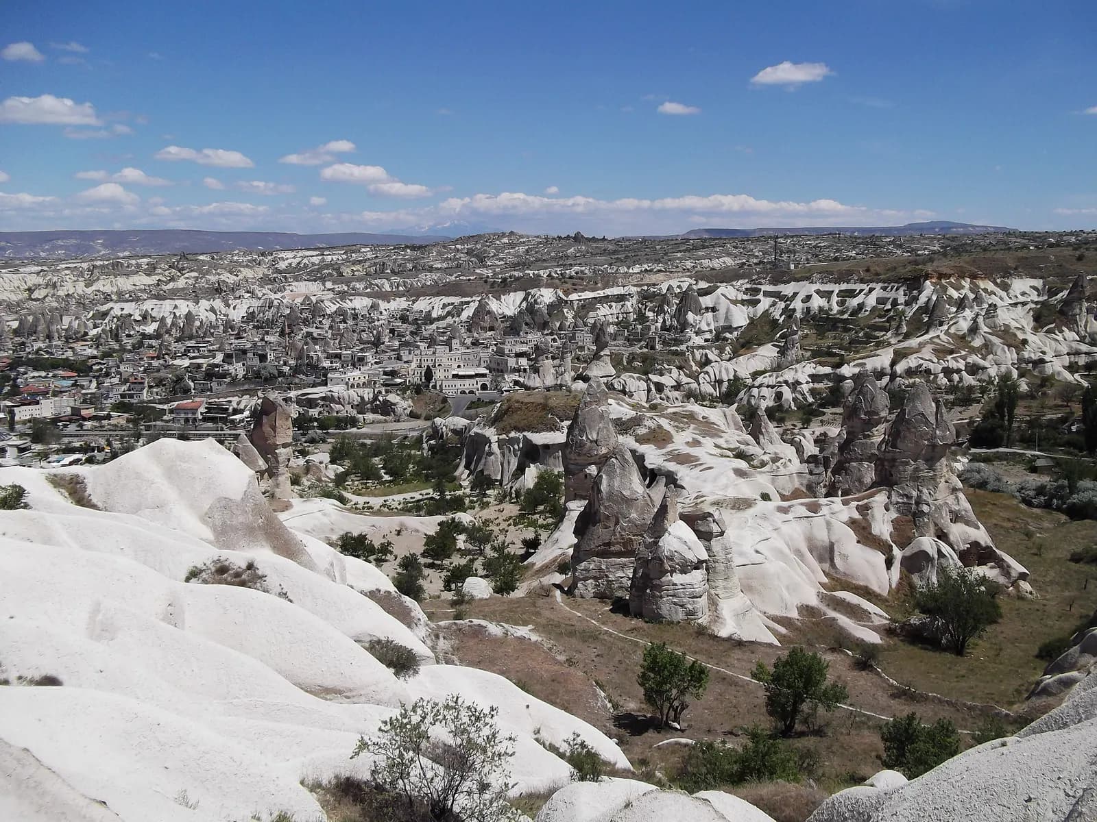 Göreme town among white rock formations and fairy chimneys, seen from a ridge above the valley under a blue sky