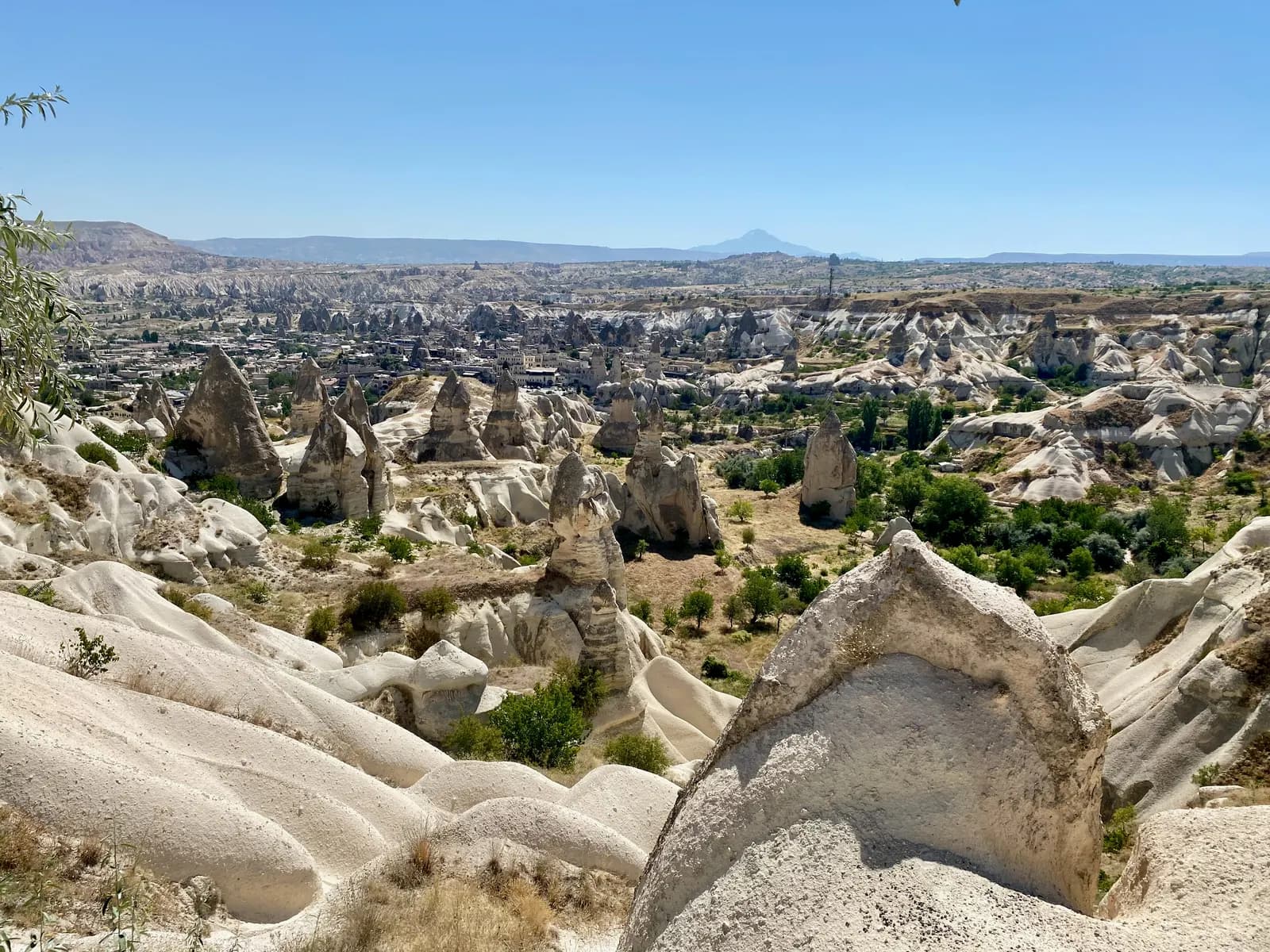 Pale rock cones and ridges in the valley around Göreme, with the town spread among the rocks and a distant mountain on the horizon