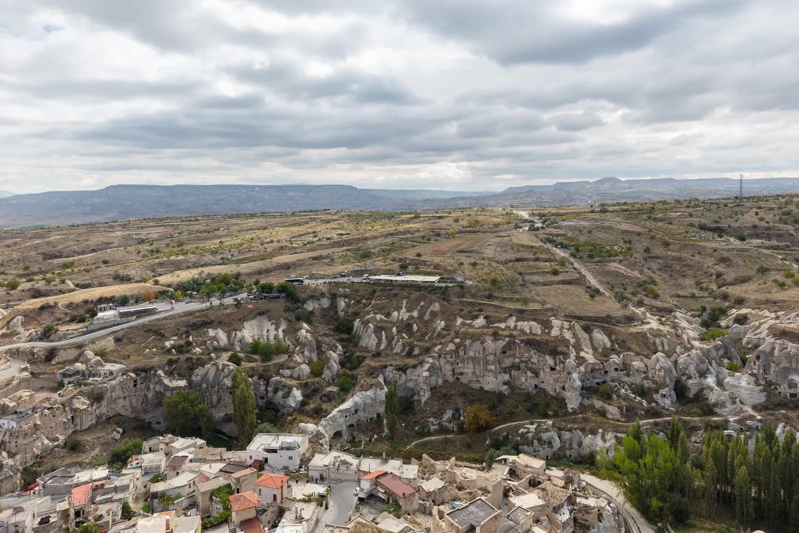 Ortahisar seen from above, with stone houses at the bottom, a valley of carved rock and a road across the plateau beyond