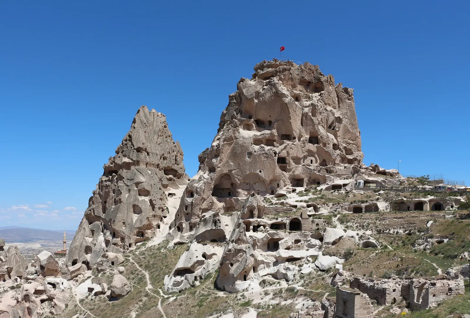 The rock of Uçhisar Castle, honeycombed with carved rooms and openings, with a Turkish flag at the top and stone houses at its foot