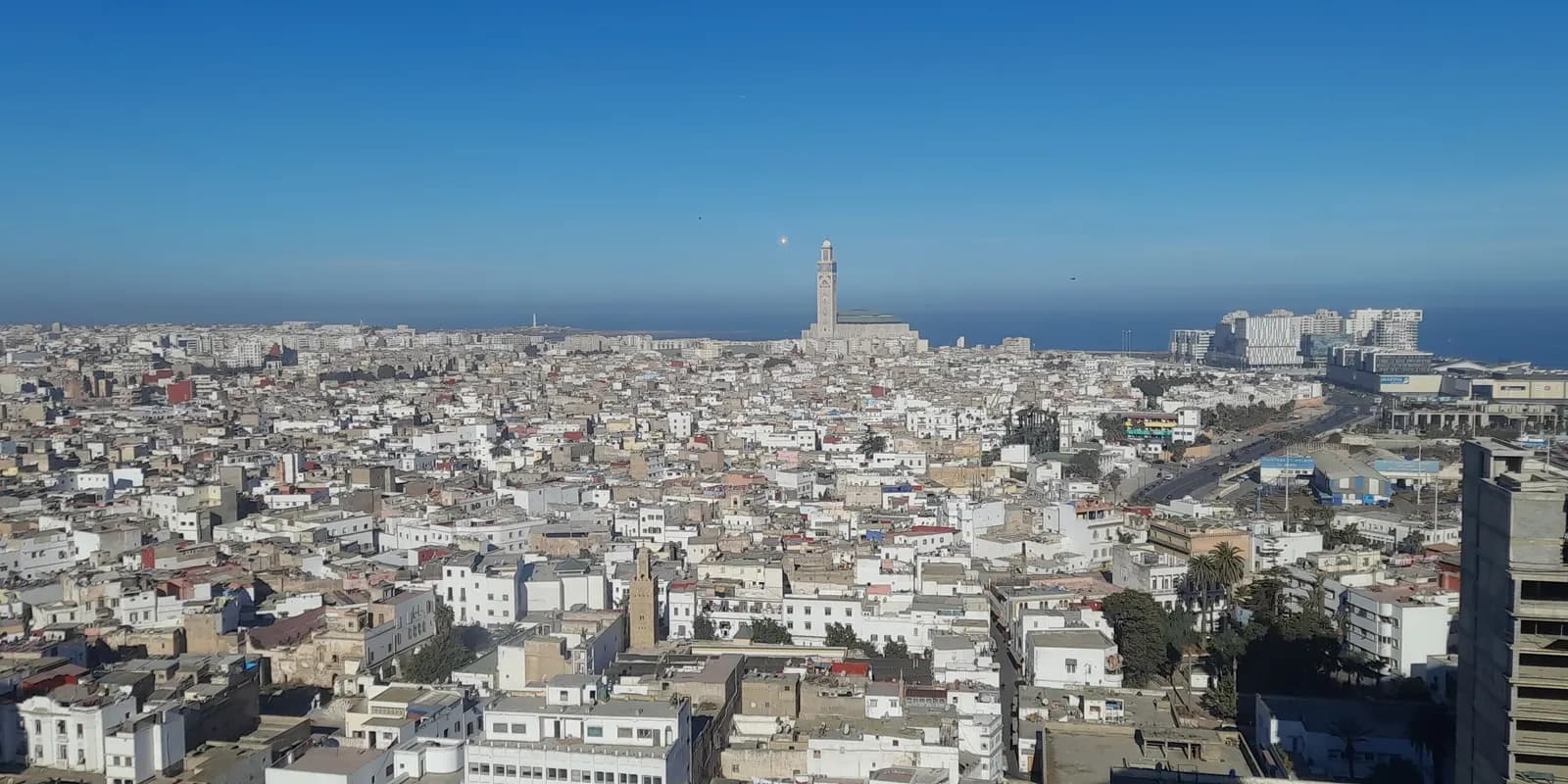 Rooftops of Casablanca's old medina on a clear morning, stretching to the minaret of the Hassan II Mosque on the Atlantic shore