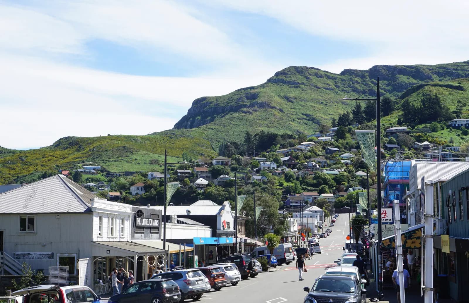 London Street in Lyttelton with cars parked along the shops and houses on the green hill behind