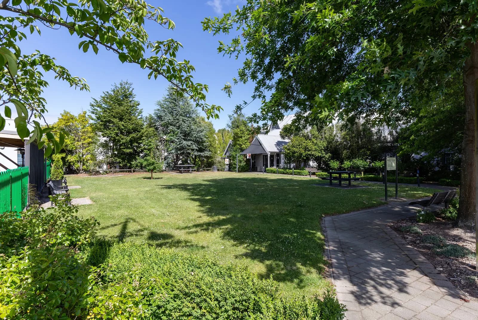 A small lawn with benches, a paved path and trees at Merivale Village Green in Christchurch