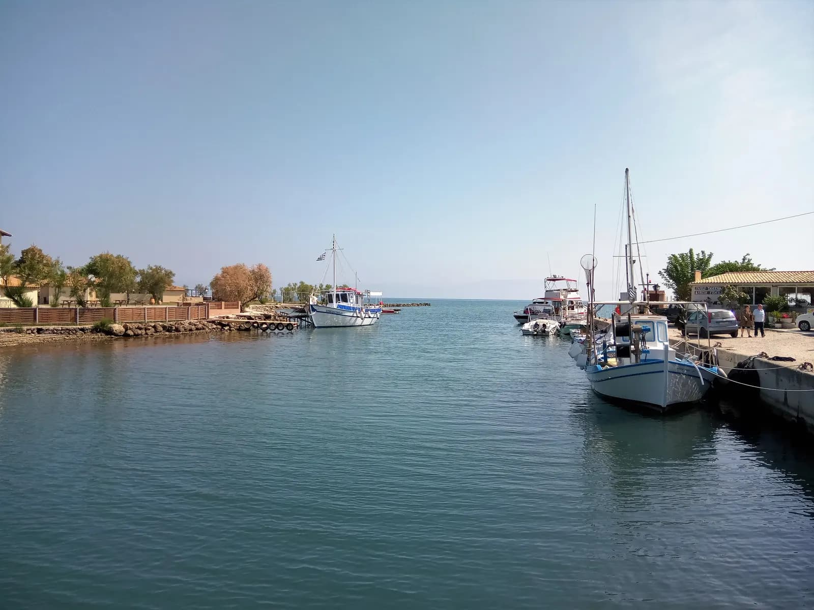 Fishing boats and tour boats moored in the river harbour at Messonghi, with houses and trees on the banks and the open sea beyond