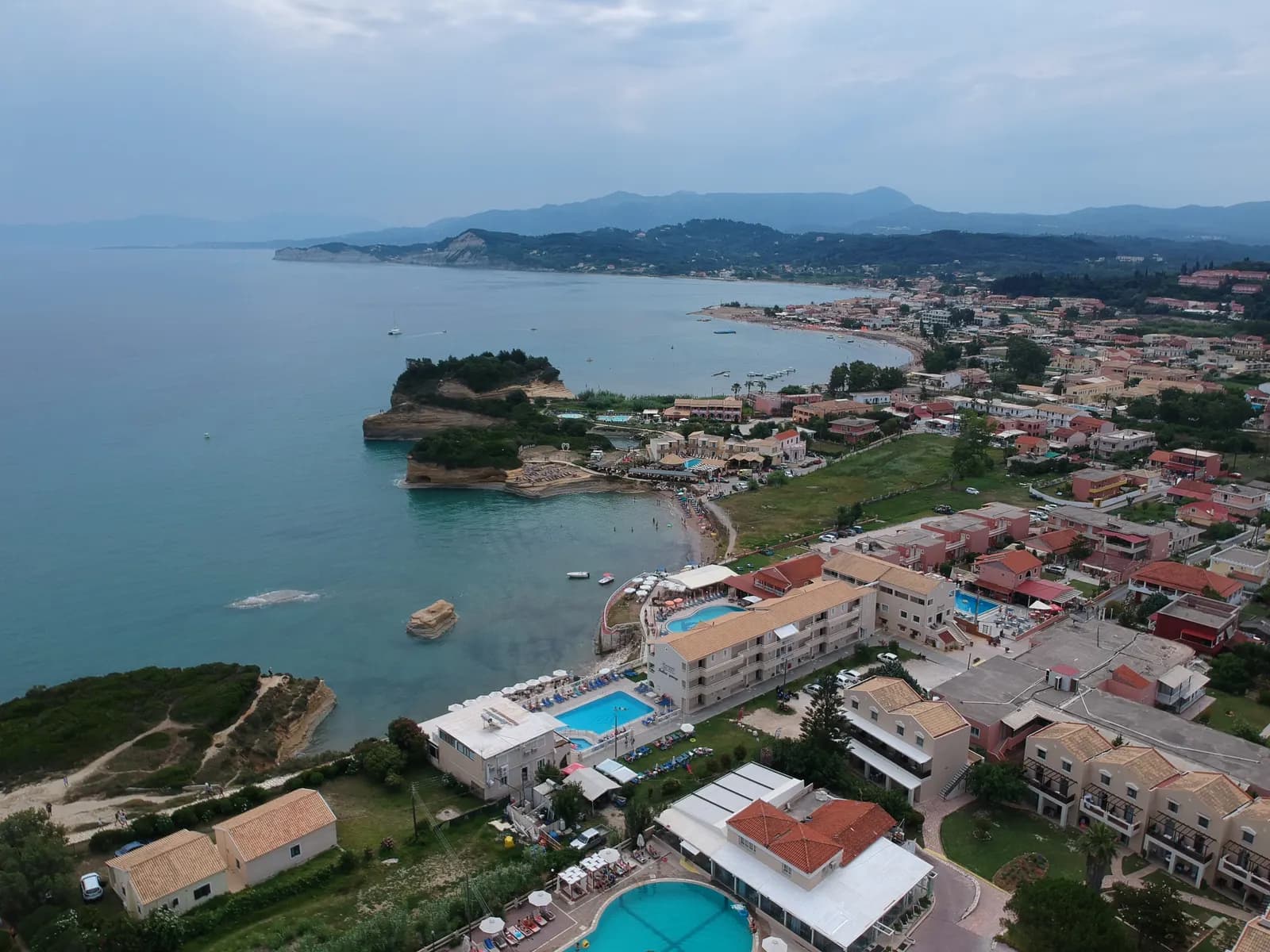 Aerial view of Sidari on the north coast of Corfu, with the sandstone headlands of the Canal d'Amour, hotels with pools and the beach curving east